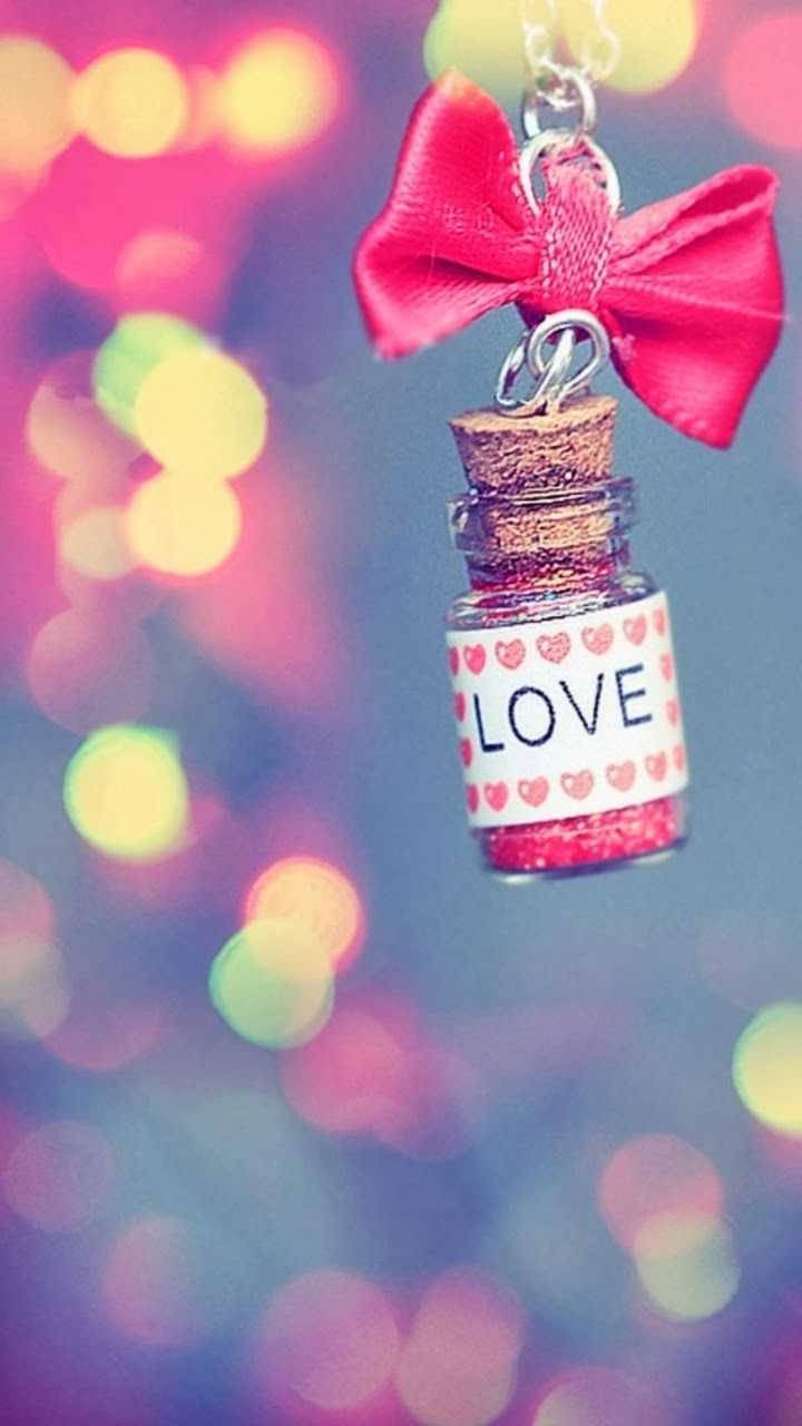 可愛少女風瓶子 壁紙 — 一個帶有紅色蝴蝶結的小閃亮瓶子，標有LOVE，懸掛在彩色散景背景前。