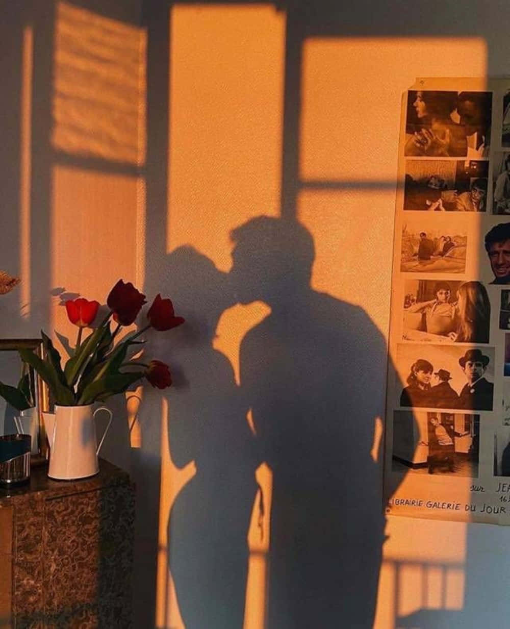 可愛情侶剪影親吻畫面 壁紙 — 溫暖的金色夕陽在牆上投射出一對情侶接吻的浪漫剪影，旁邊有紅色鬱金香和復古照片。