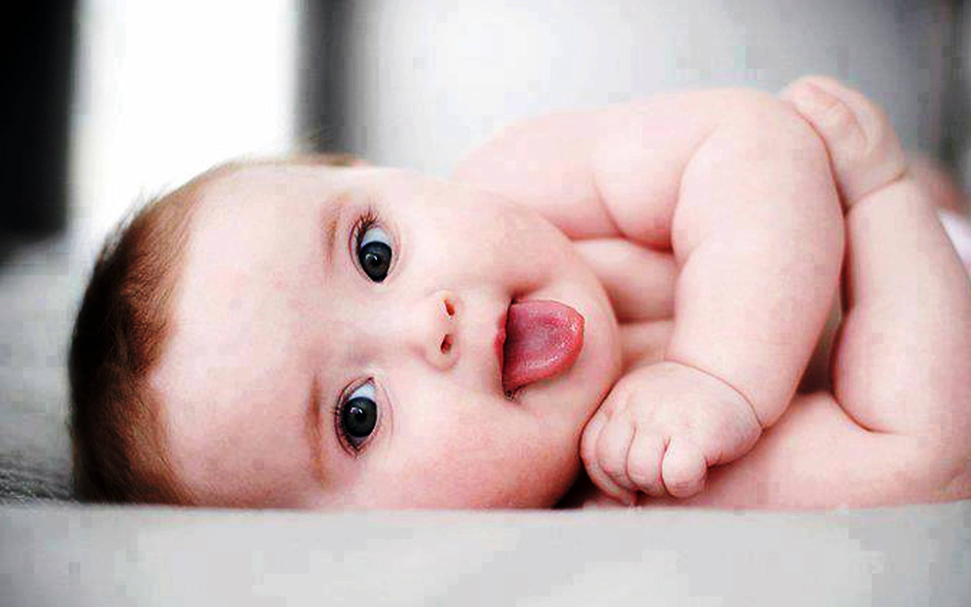 可愛搞笑嬰兒 壁紙 — 一個胖嘟嘟嘅BB，有對大黑眼，喺軟表面上面攤開背脊伸脷。