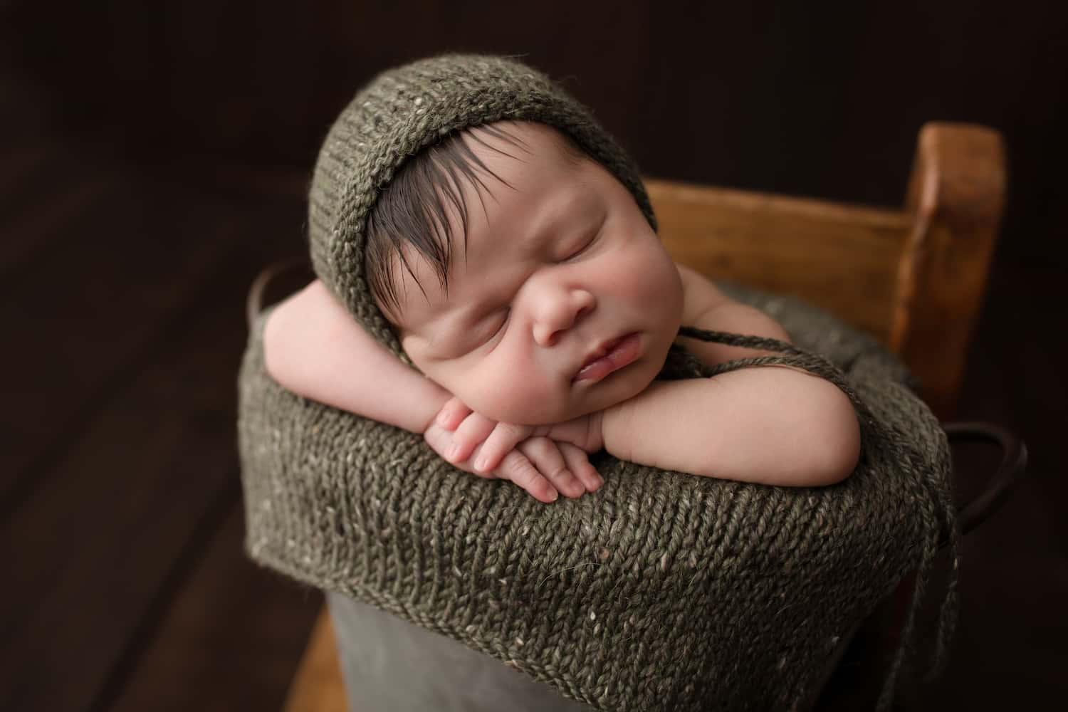 一個在木桶中包裹著橄欖綠色針織布料睡覺的新生嬰兒。