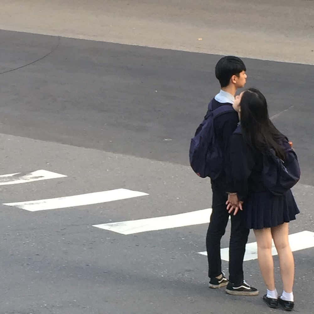 可愛時尚情侶學生照 壁紙 — 兩名穿著校服的學生在行人過路處上緊密地站著，手牽手一起向前凝視。