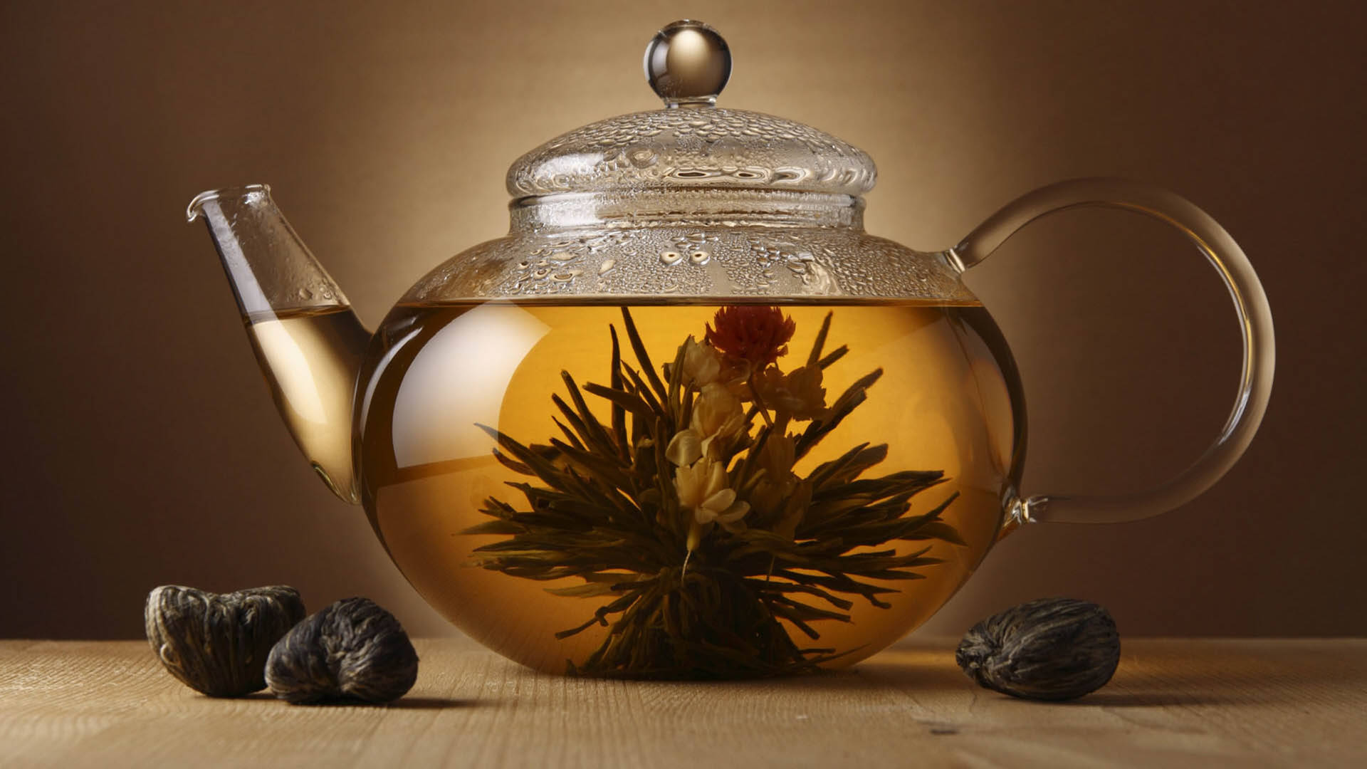 玻璃茶壺、盛開的茶和乾茶球在木桌上。