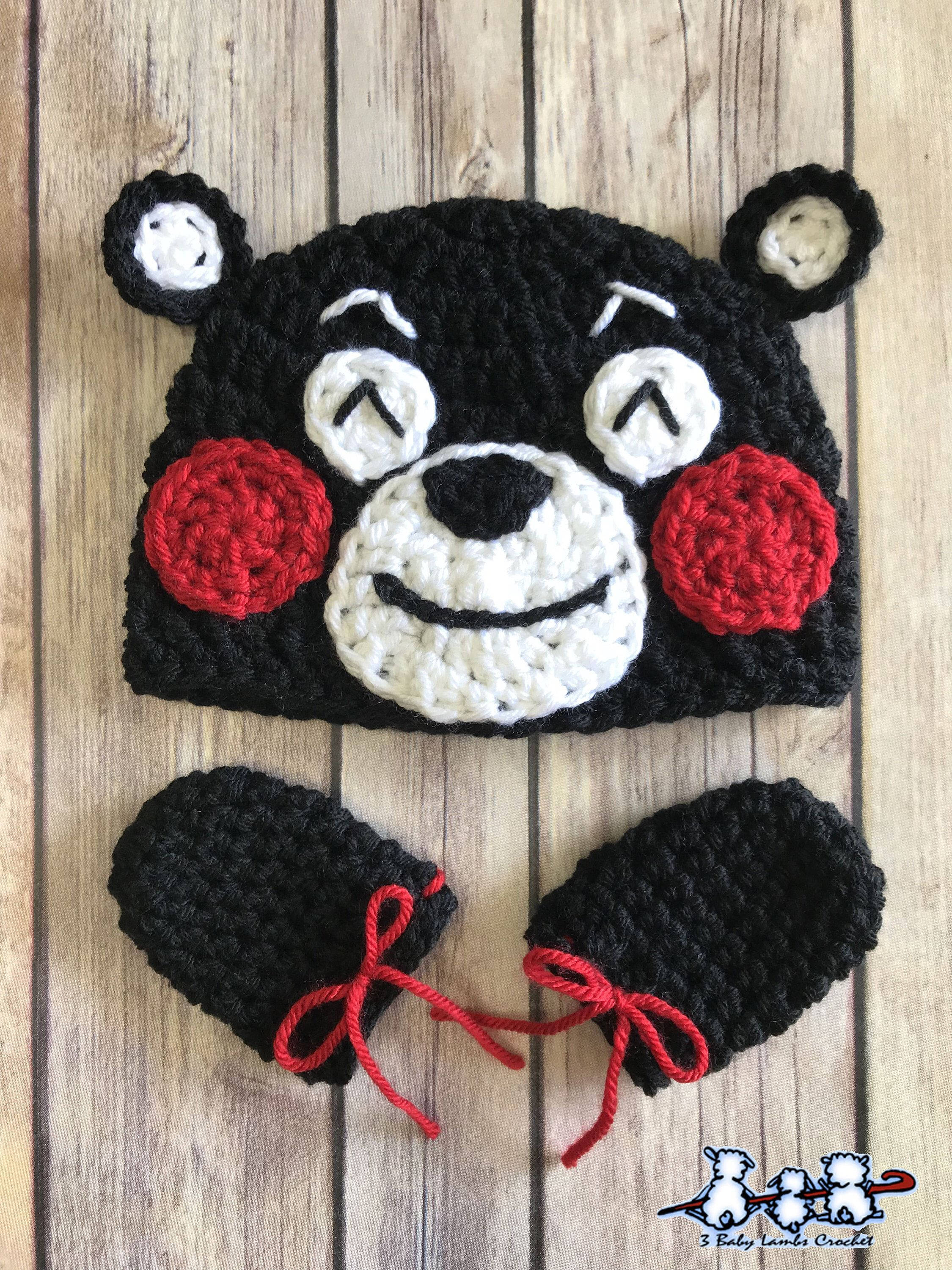 可愛熊本熊編織品 壁紙 — 一頂手工製作的黑色鉤針編織熊帽，配有紅色臉頰和相配的連指手套，放在木質表面上。