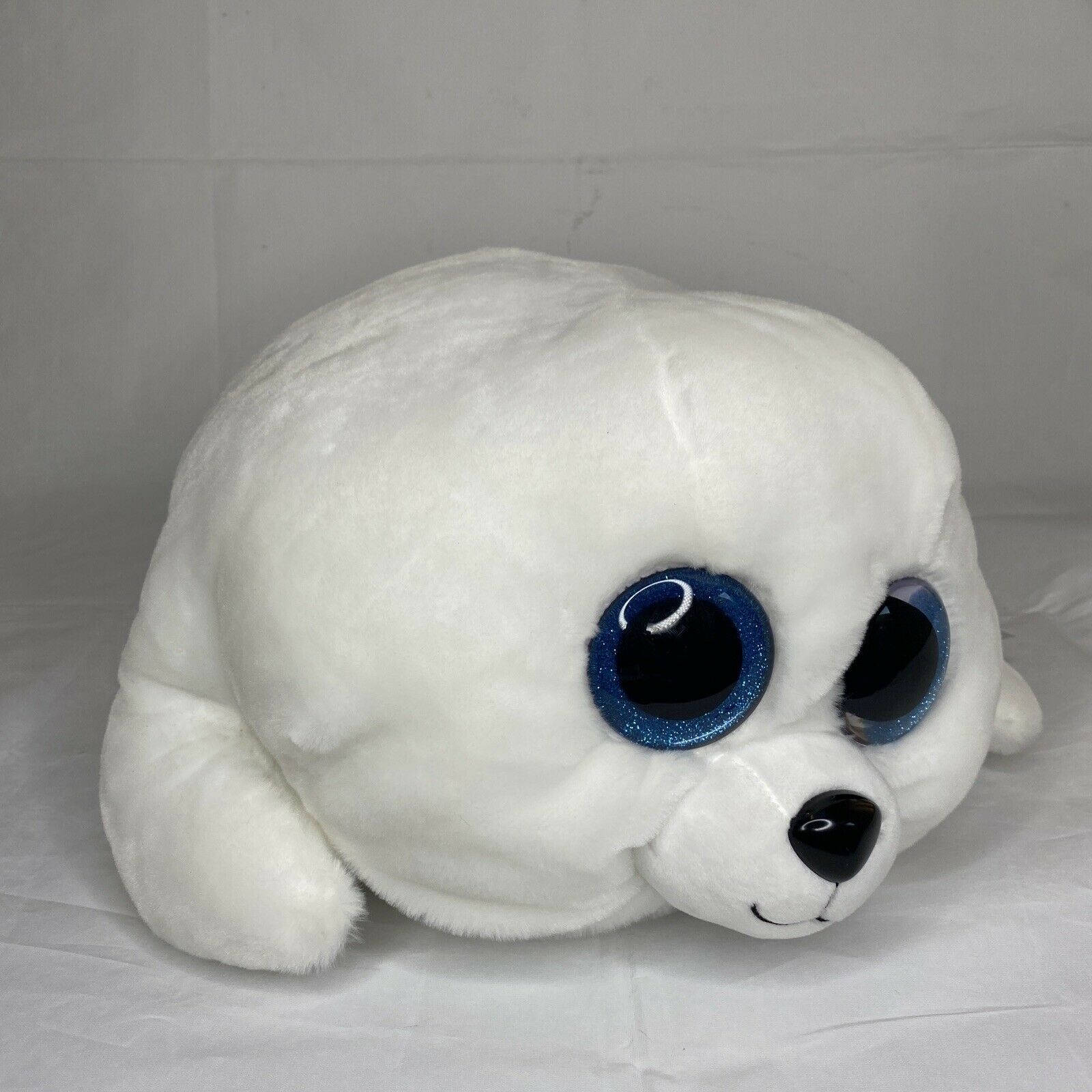 可愛白色絨毛Beanie Boos玩偶壁紙 壁紙 — 一隻毛茸茸的白色毛絨海豹，閃爍著藍色眼睛，躺在純白色的表面上。