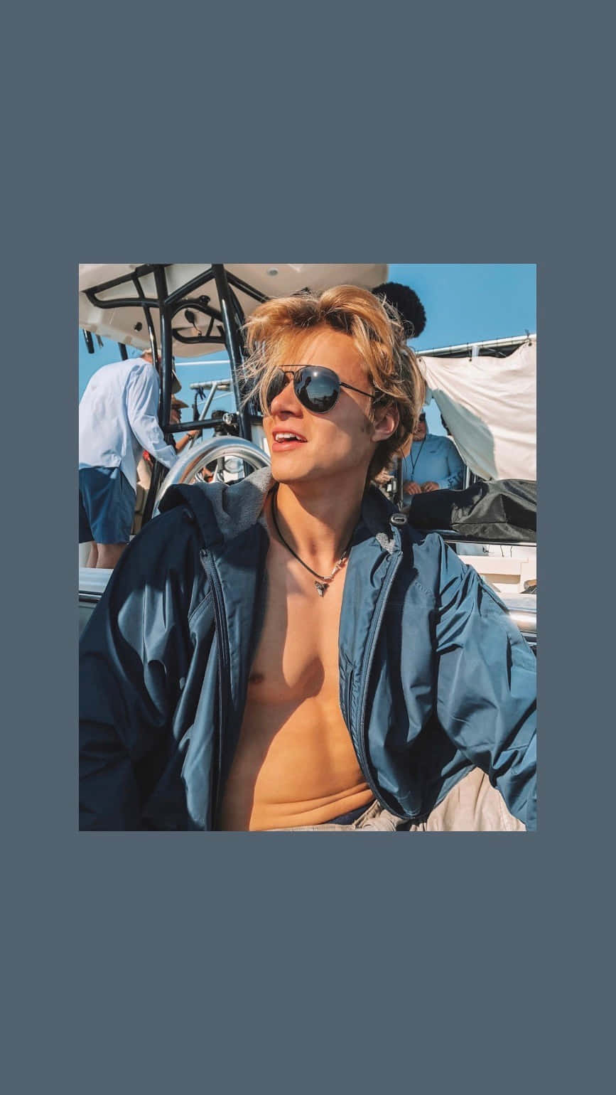 戴太陽眼鏡和藍色外套的年輕男子在夏日陽光下於船上微笑。