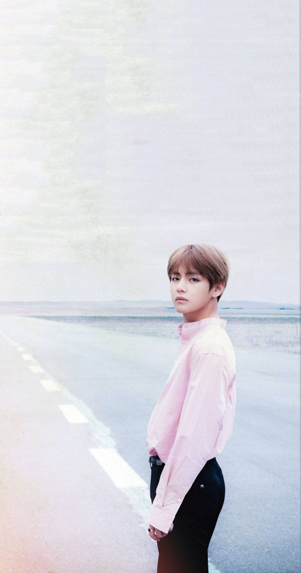 可愛的BTS V在海灘 壁紙 — 一名身穿粉紅色襯衫的年輕男子獨自站在一條空曠的長路上，天空朦朧。
