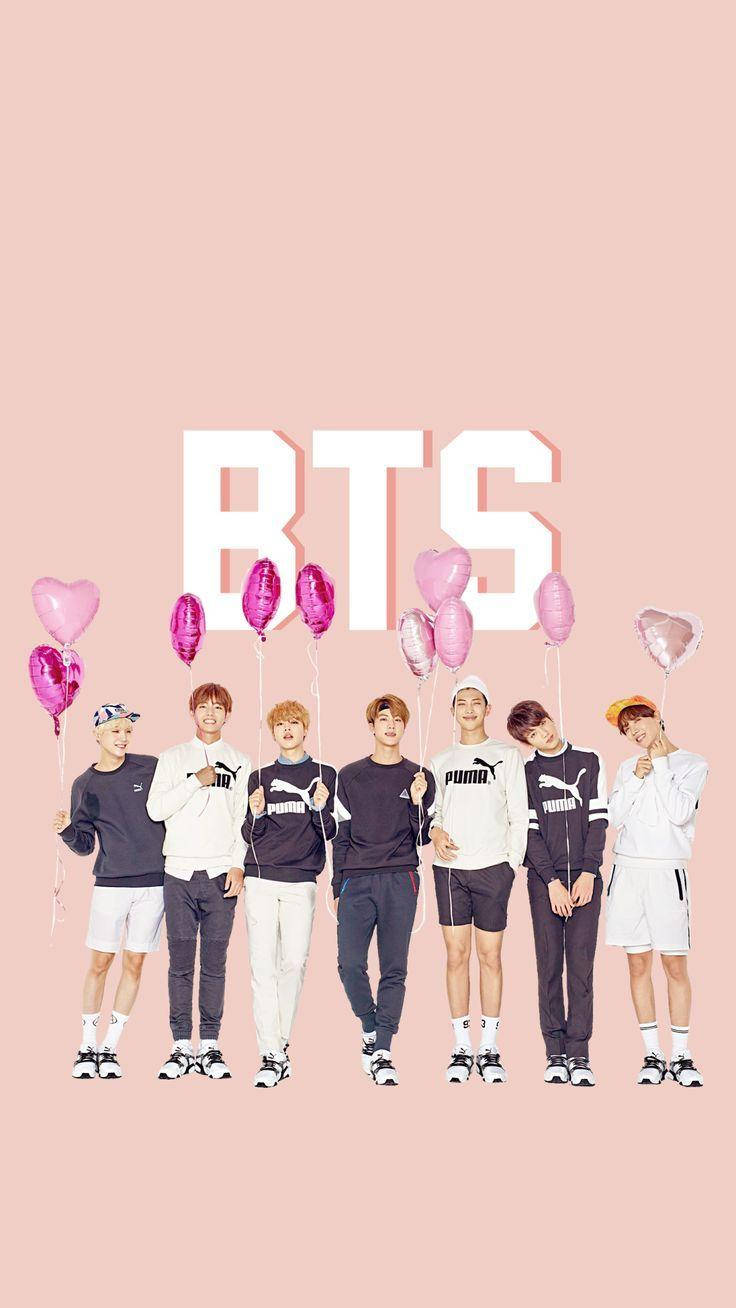 可愛的BTS手持心形氣球 壁紙 — BTS 七名成員站成一排，手持粉紅色心形氣球，背景為柔和粉紅色，上方有大型白色「BTS」字母。