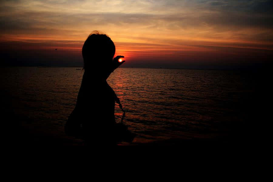 孩子剪影在水邊觸碰夕陽。