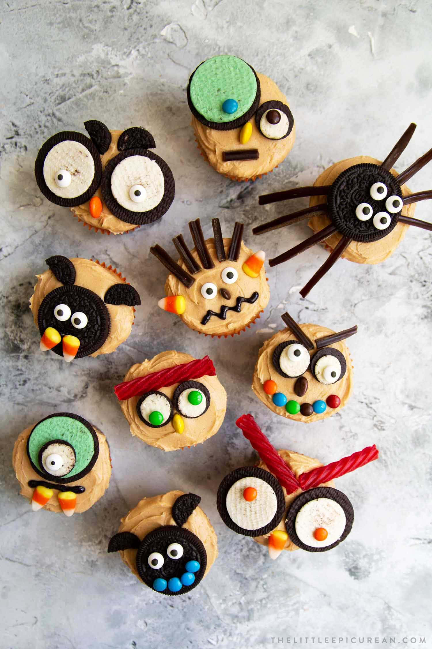 Halloween Cupcakes 桌布 壁紙 — 可愛的萬聖節杯子蛋糕，用Oreo餅乾、糖果眼睛和彩色糖果裝飾成恐怖生物，放在灰色表面上。