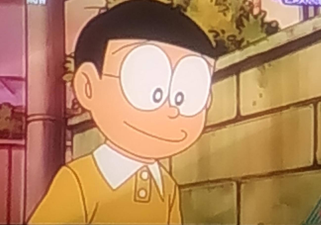動畫角色，有大眼睛和黃色襯衫，在磚牆附近微笑。