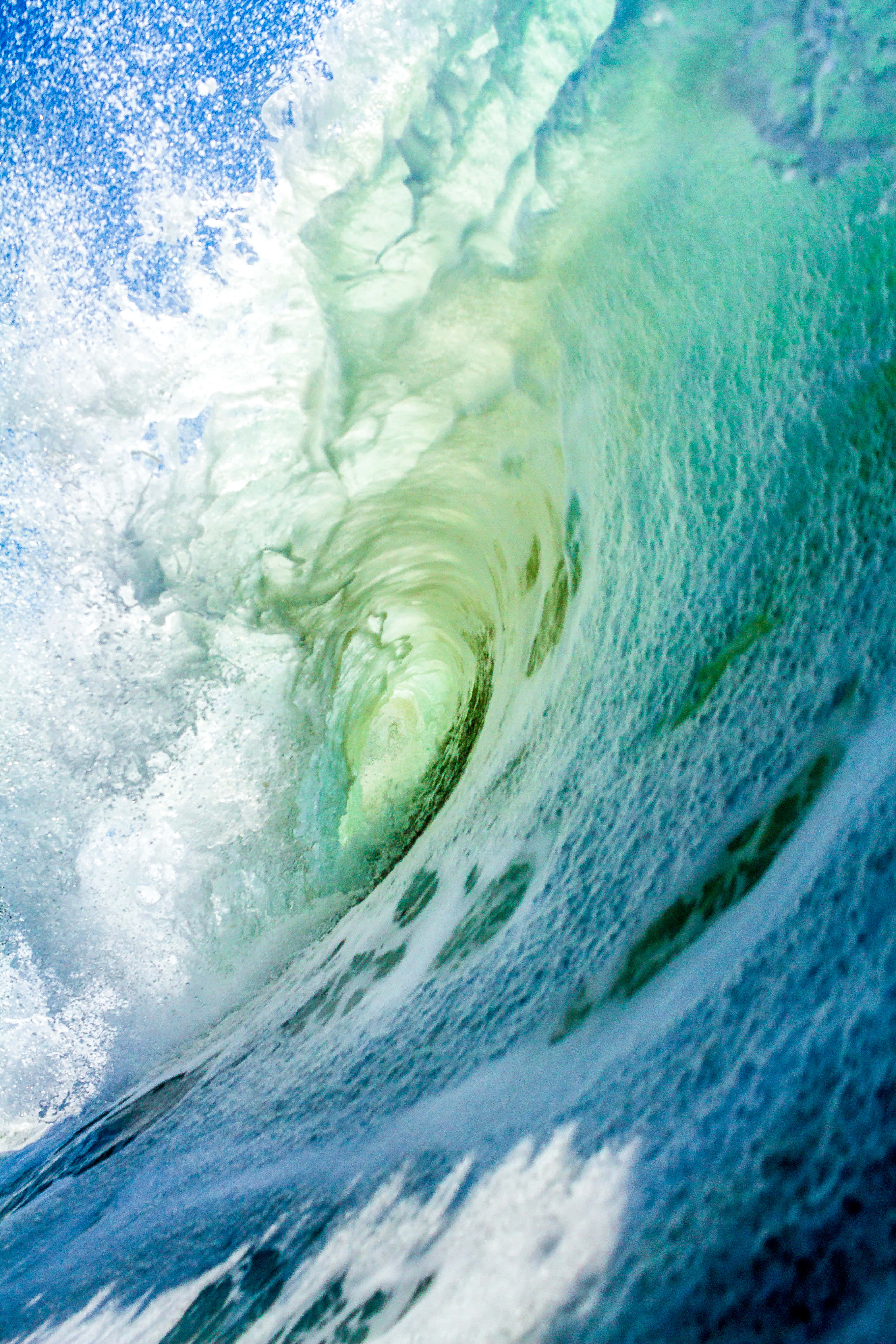 可愛的青綠色iPhone大海波浪壁紙 壁紙 — 一道強勁的海浪捲成半透明的綠色隧道，帶有白色泡沫，襯托著明亮的藍天。