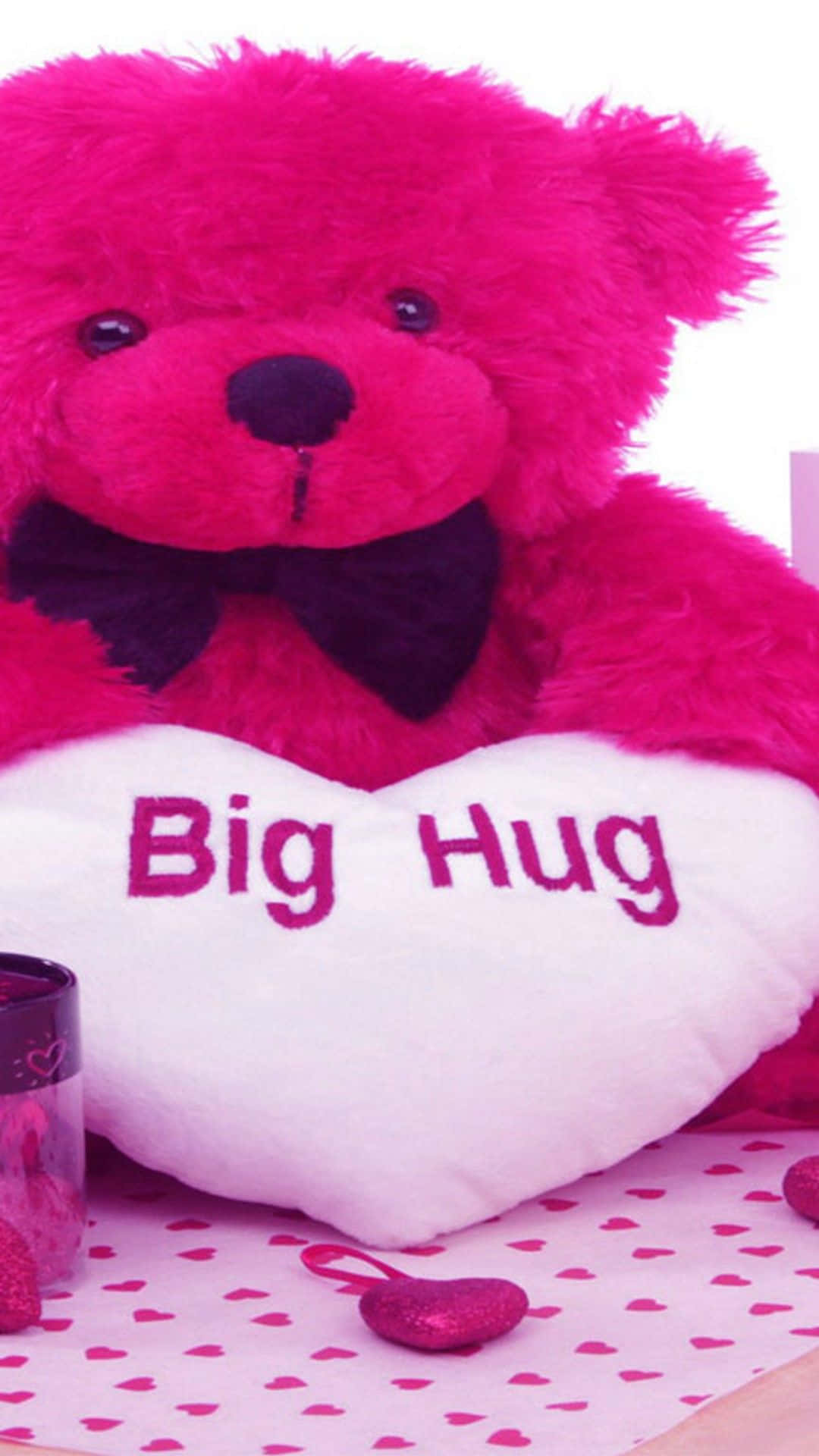 粉紅色泰迪熊在粉紅色心形圖案背景上抱著一個寫有「Big Hug」的白色心形枕頭。