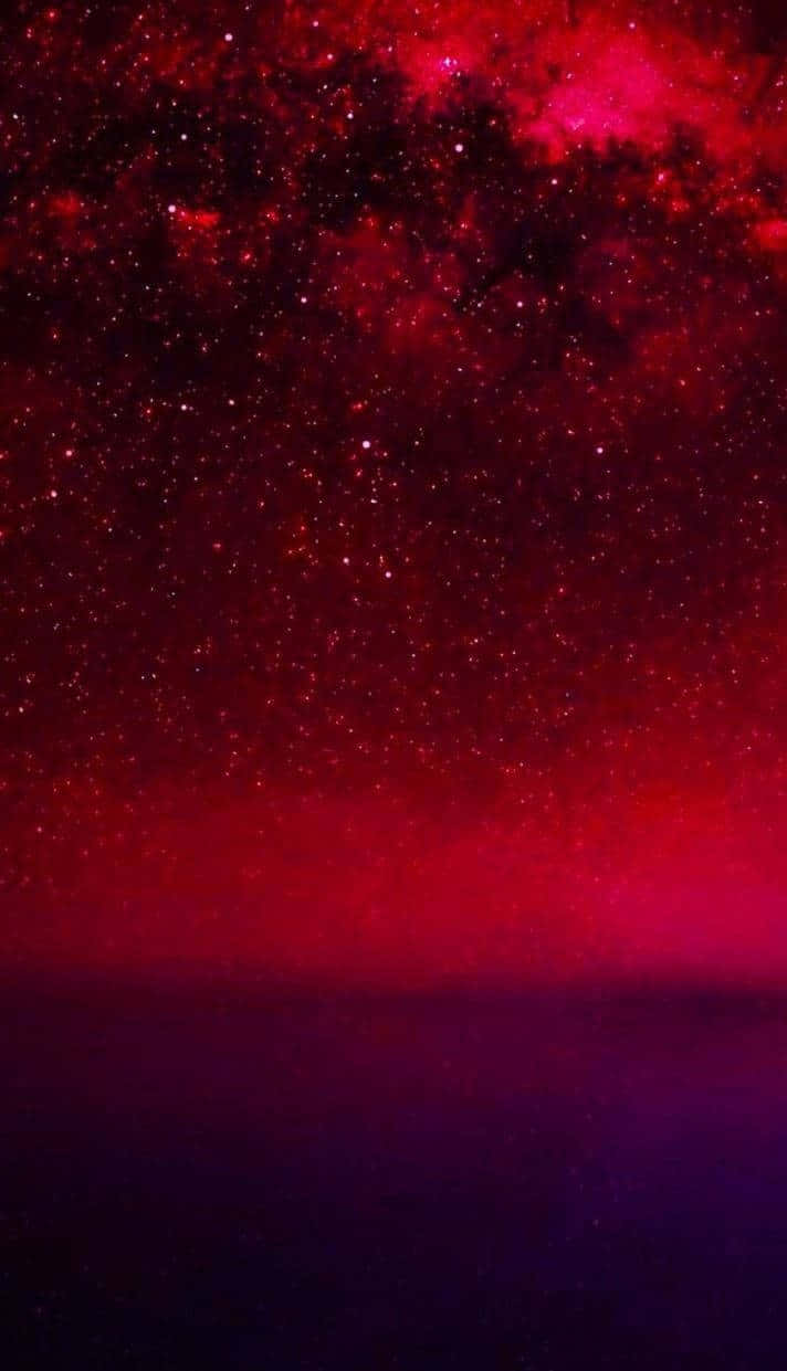 在黑暗地平線上方，充滿恆星和宇宙塵埃的鮮豔紅色星系。