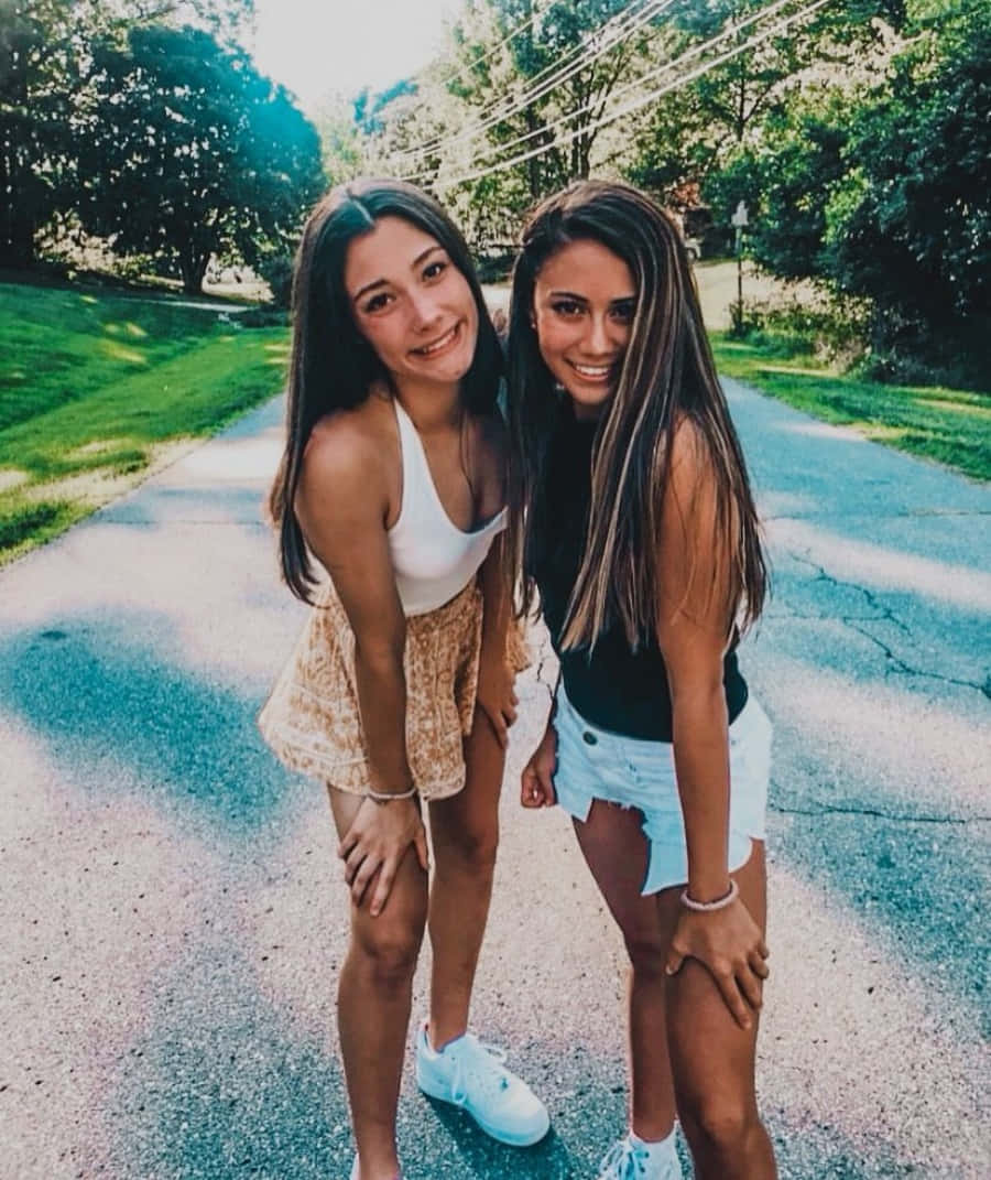 兩位年輕女性在陽光明媚的戶外小路上微笑並一起擺姿勢。