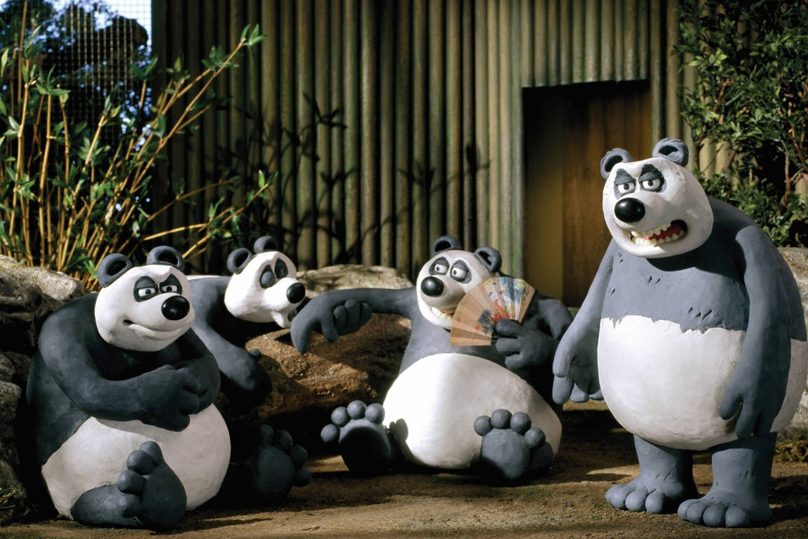 四個黏土動畫熊貓雕像在動物園圍欄內，有竹子。