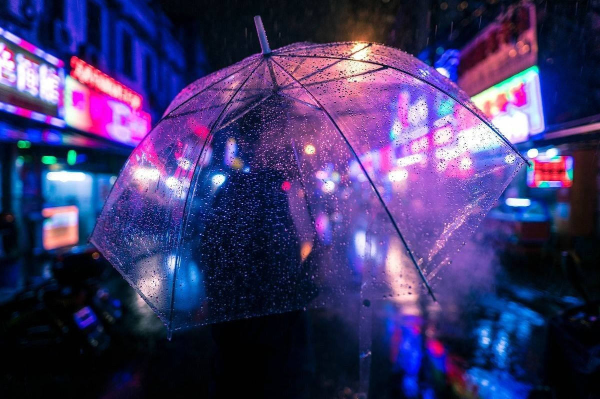 可愛靛藍美學燈光 壁紙 — 一把透明雨傘佈滿雨點，在夜晚濕漉漉的城市街道上折射霓虹燈光。
