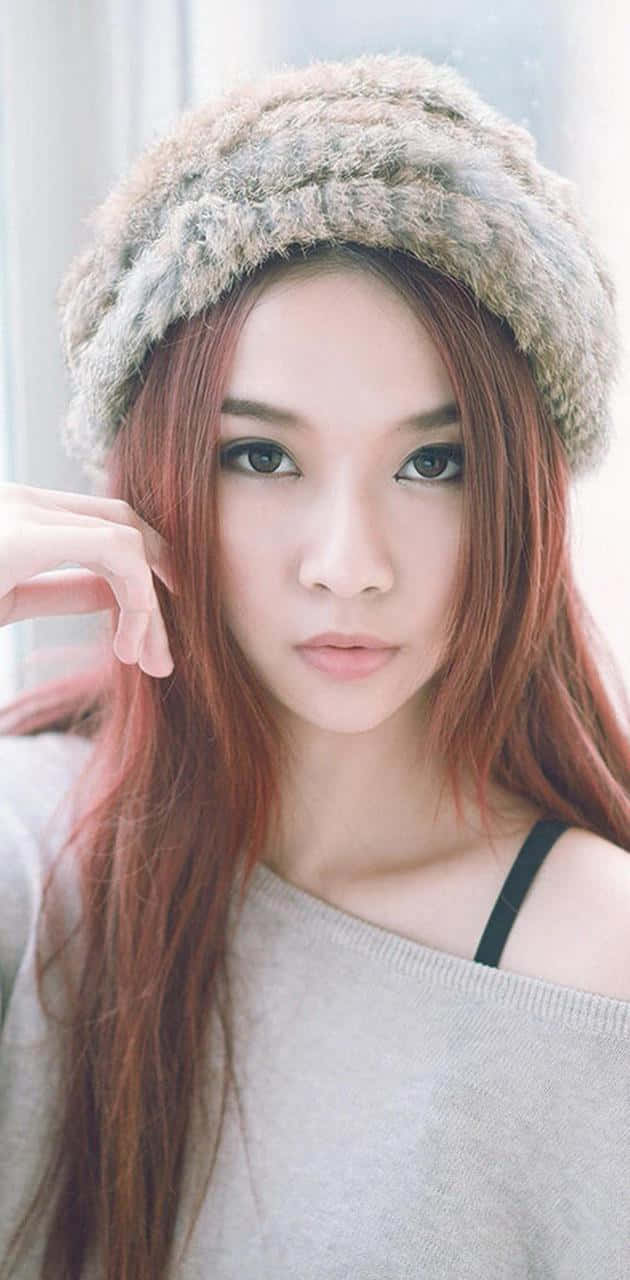 可愛韓國女孩戴帽露肩寫真 壁紙 — 一位長紅髮的年輕女性戴著毛絨絨的米色帽子，在明亮的窗邊房間裡溫柔地凝視著相機。