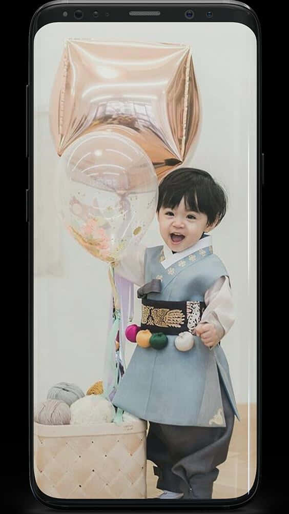 可愛韓國幼童穿韓服拿氣球寫真 壁紙 — 一個快樂的幼兒穿著傳統韓服，拿著玫瑰金和透明的五彩紙屑氣球，旁邊放著一籃紗線。