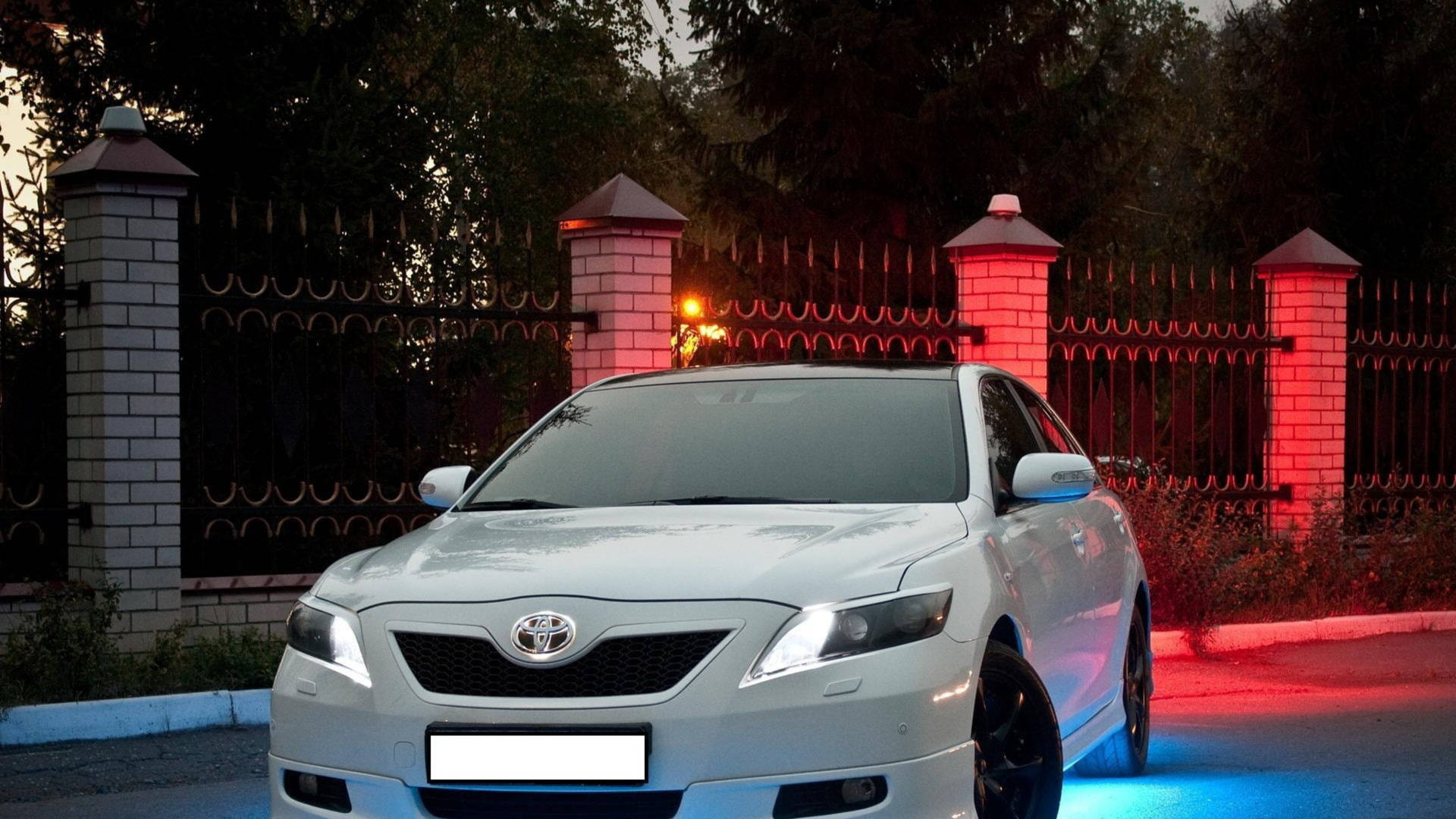 銀色豐田Camry在黃昏時停泊，車輪下發出紅色和藍色的霓虹燈光。