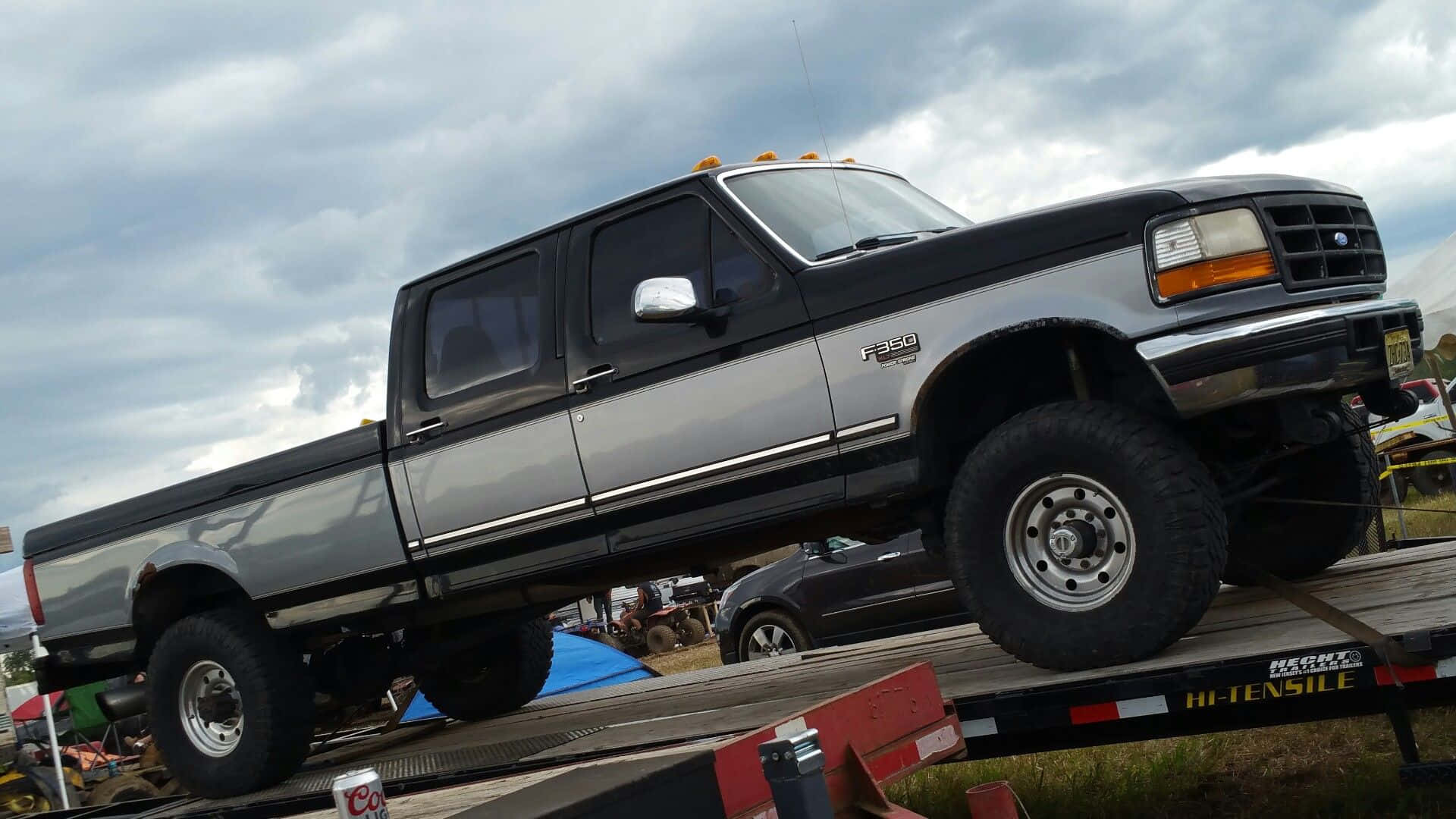 喺戶外活動中，一架升高嘅黑色同銀色福特F-350皮卡車喺平板拖車上。