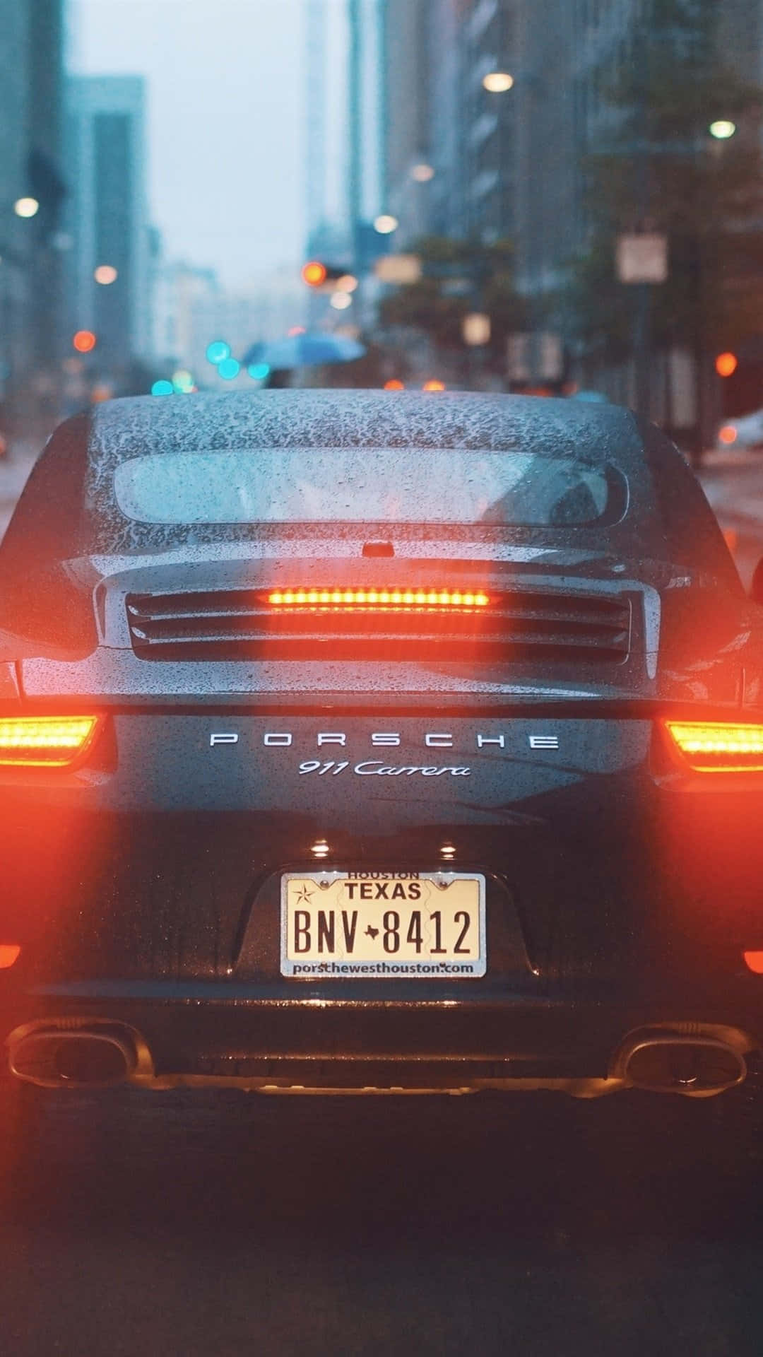 黑色保時捷911 Carrera，紅色尾燈，在雨城市街黃昏行駛。