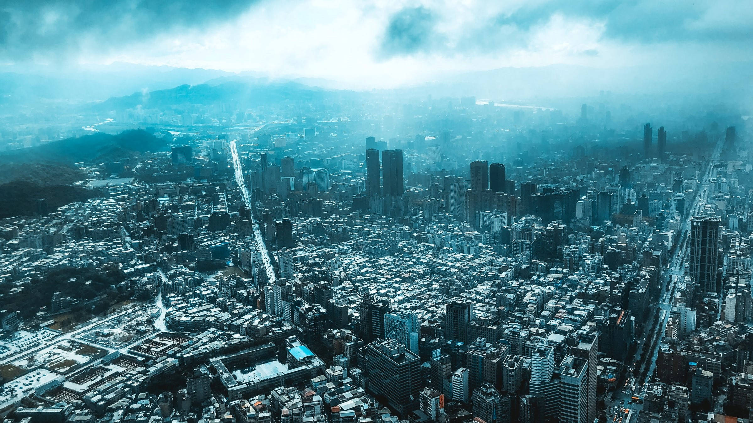 台北101塔樓城市景觀 壁紙 — 在陰鬱的藍天下，遠山和朦朧雲層中廣闊城市景觀的鳥瞰圖。