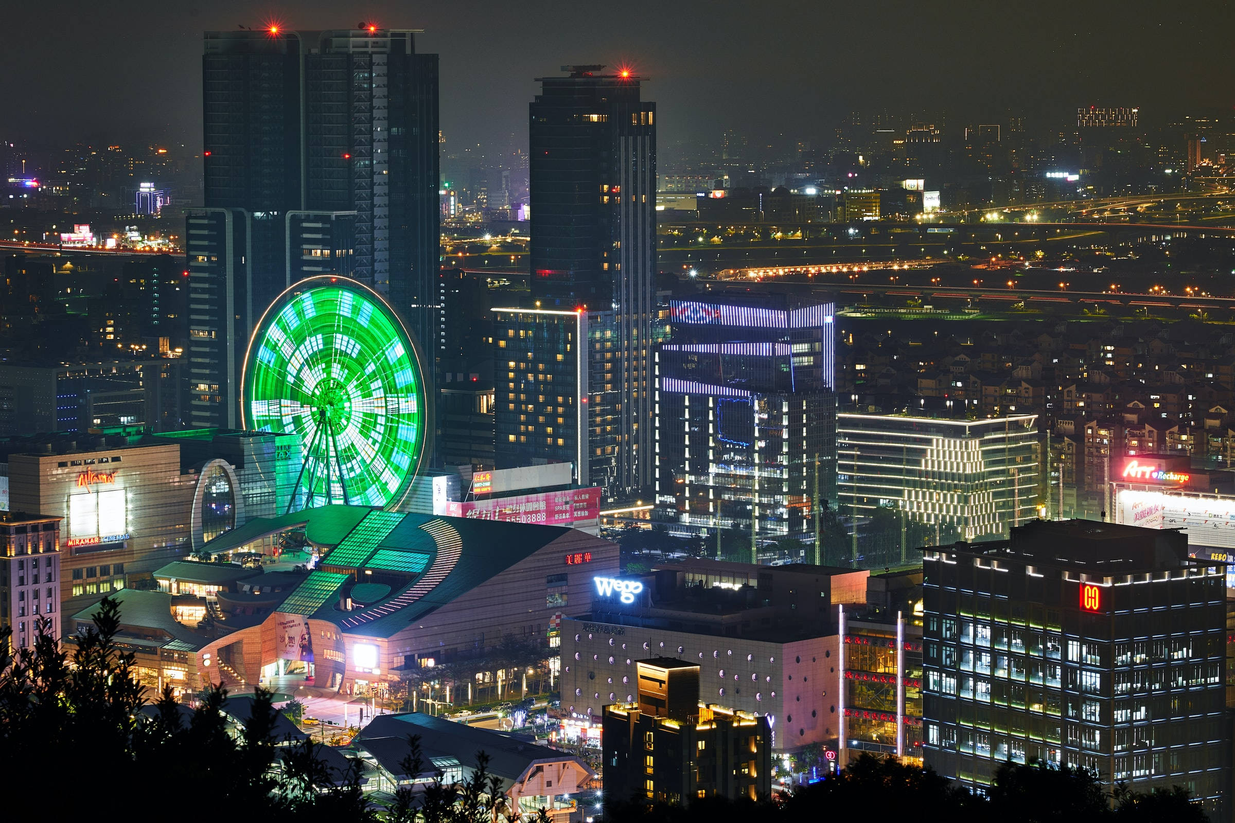 台北夜景與摩天輪 壁紙 — 一個令人眼花繚亂的夜間城市景觀，在摩天大樓和充滿活力的霓虹燈中，有一個發光的綠色摩天輪。
