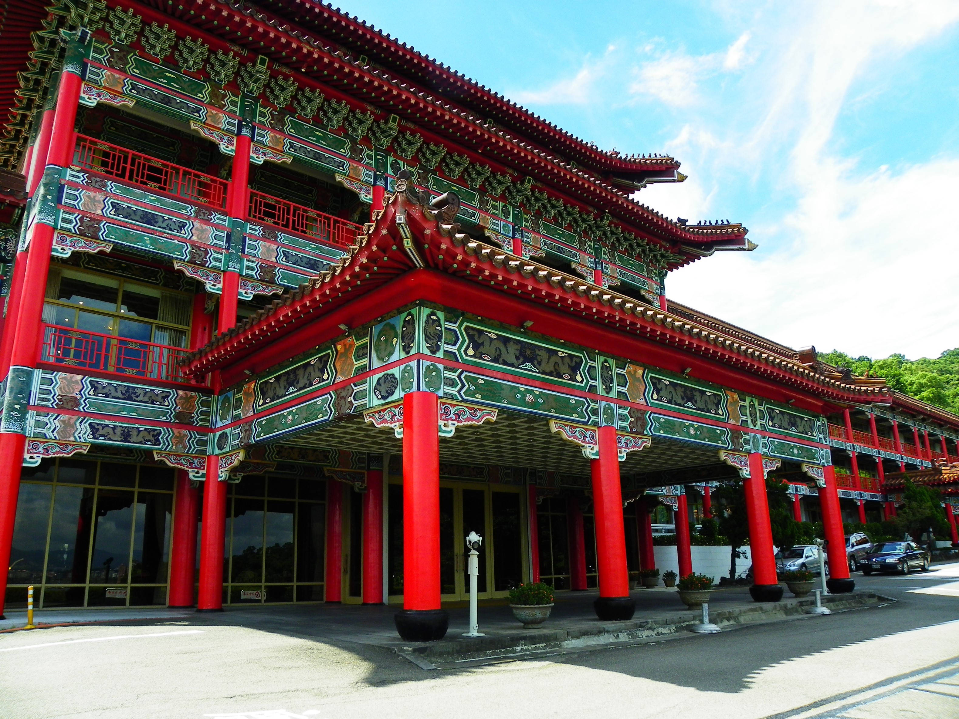 台北大飯店麒麟廳 壁紙 — 一座宏偉的傳統中國寺廟，擁有鮮紅色的柱子和華麗的綠色屋頂邊緣，在明亮的藍天下。