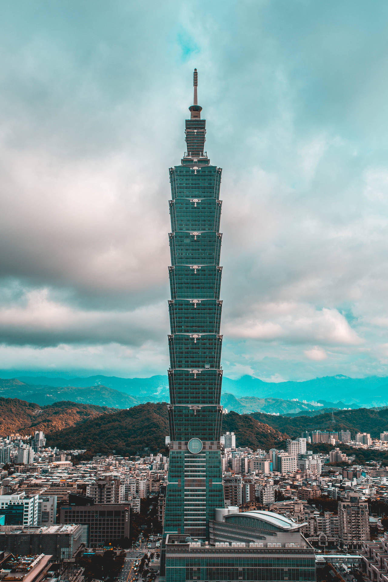 台北101摩天大樓聳立在密集的城市之上，背景有山脈。