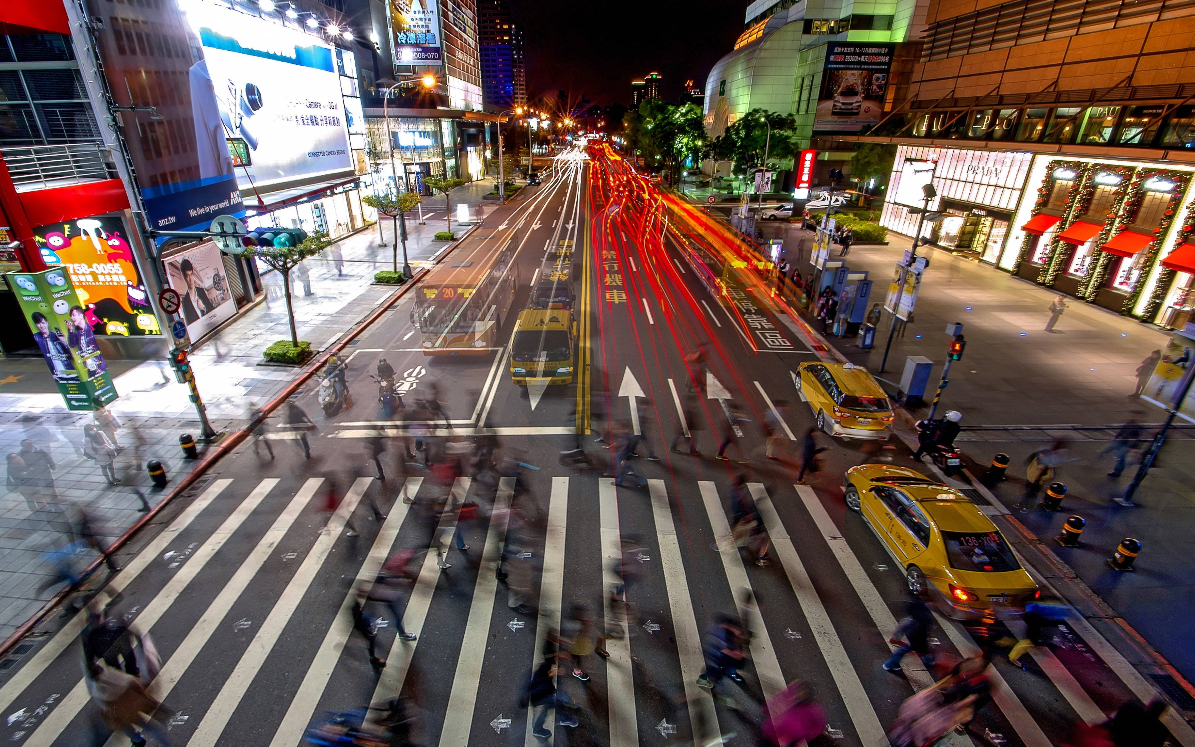台北市街景 壁紙 — 從高角度拍攝的繁華城市街道夜景，帶有紅色車燈軌跡和模糊的行人正在過斑馬線。