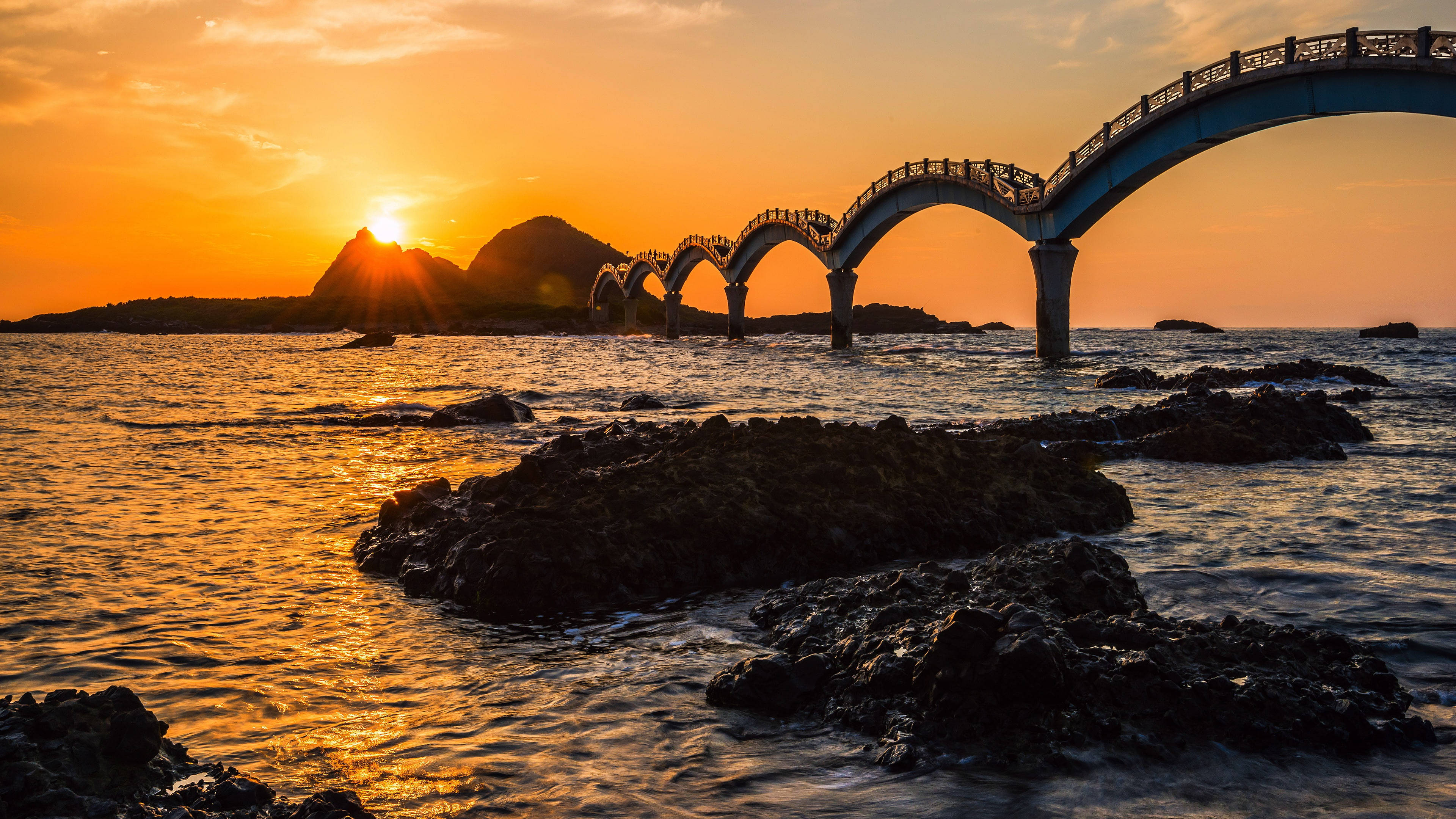 台灣三仙台拱橋 壁紙 — 海洋上壯麗的日落，長拱橋在熾熱的橙色天空和漣漪水面上形成剪影。