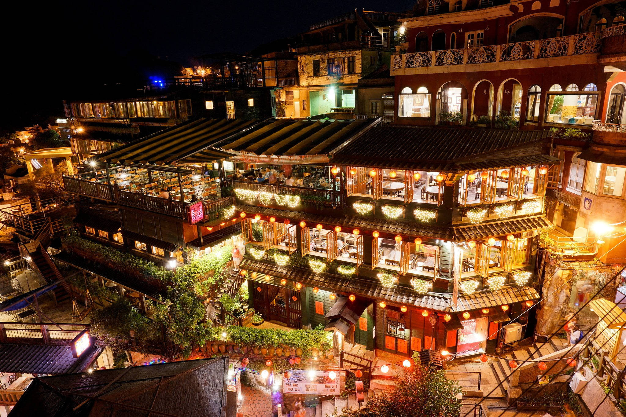 台灣九份老街 壁紙 — 一個充滿活力的夜景，多層露台餐廳散發著溫暖的光芒，依偎在山坡上。