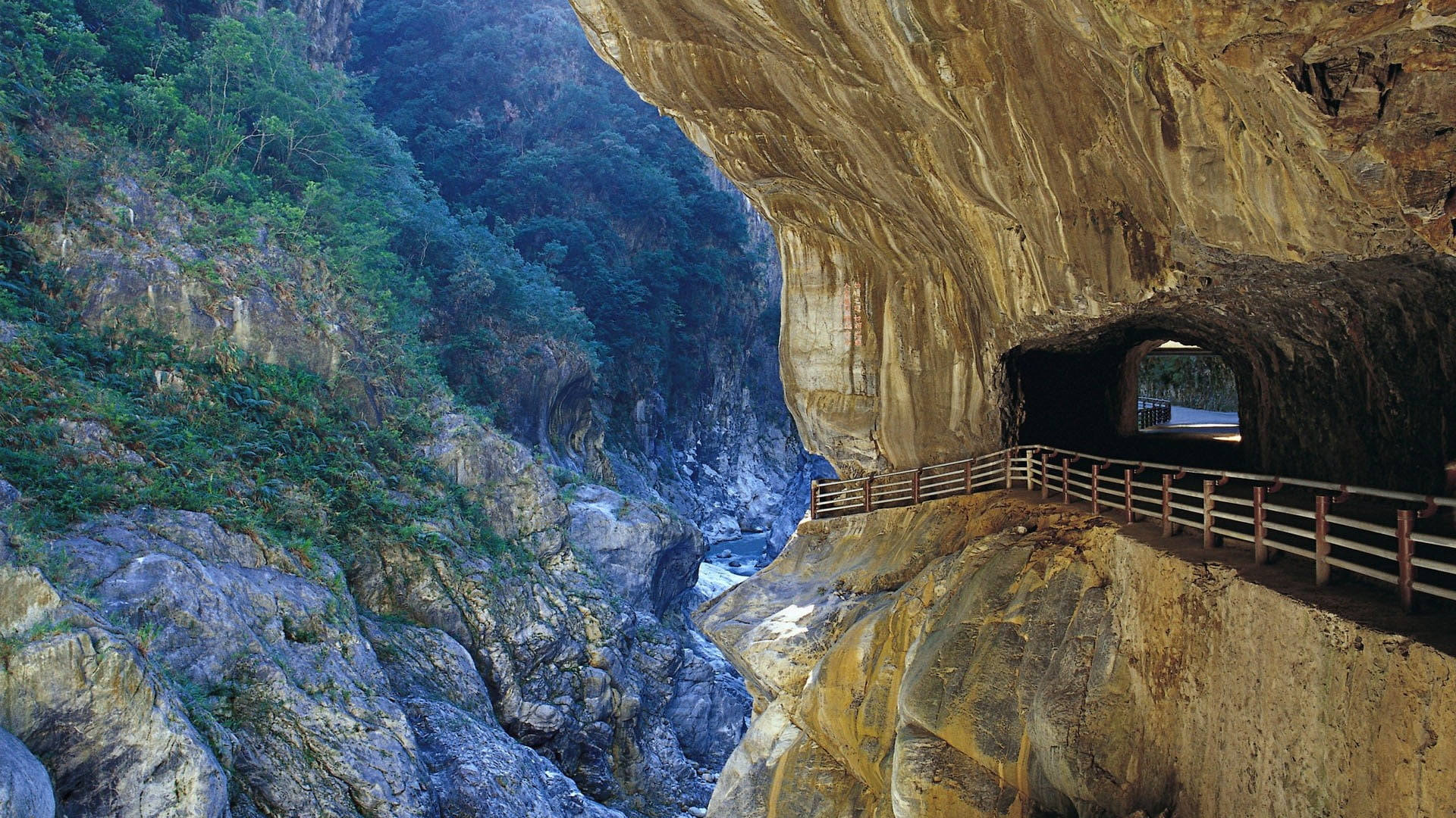 台灣九彎隧道 壁紙 — 一條蜿蜒的木棧道緊貼著巨大岩石突出部分，下方是深峽谷和湍急的河流。