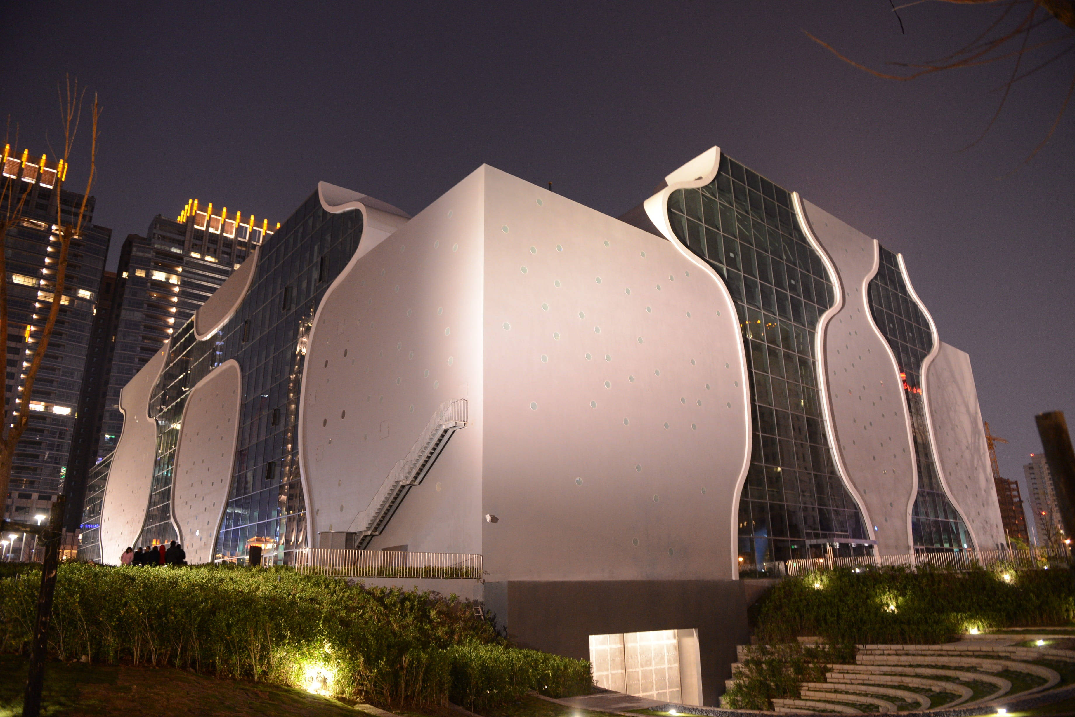 台灣台中歌劇院 壁紙 — 一座未來主義的白色建築，帶有流暢的曲線和玻璃面板，在夜晚的黑暗天空和背景城市燈光中閃耀。