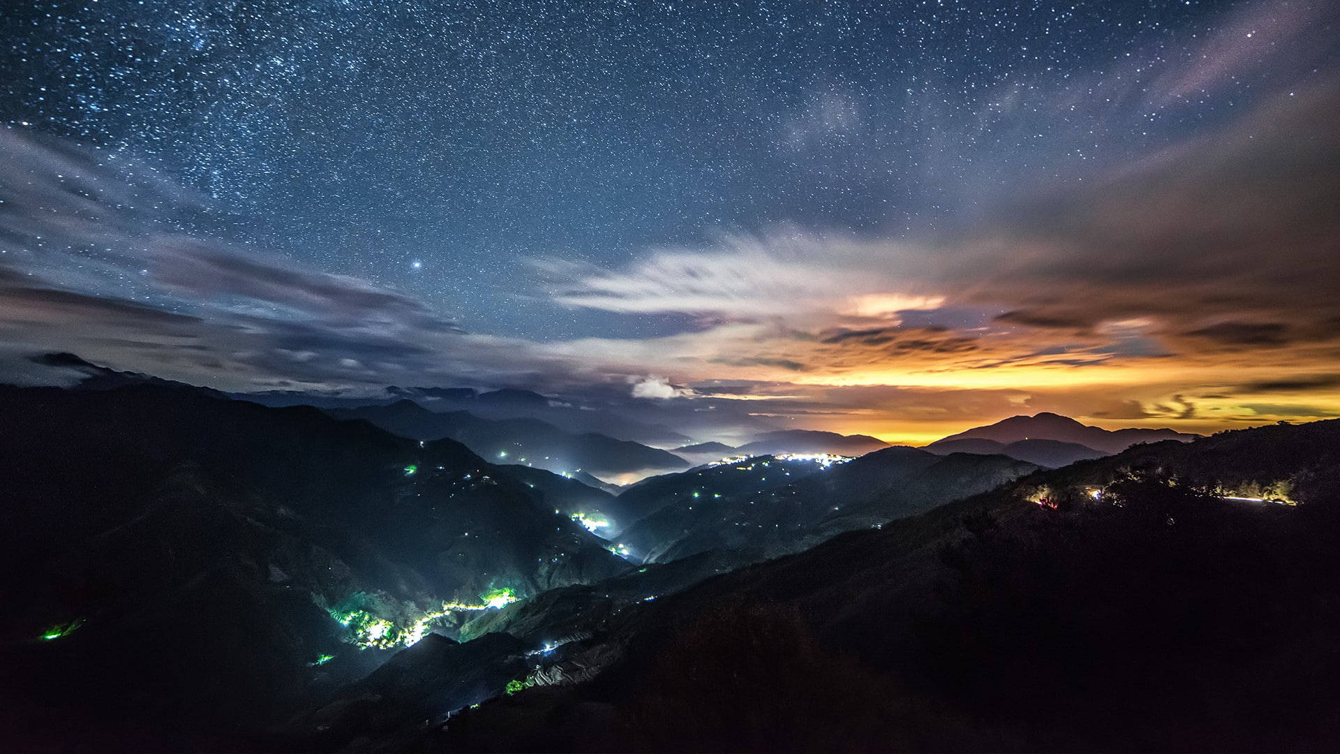 台灣合歡山 壁紙 — 繁星點點的夜空拱形籠罩著層疊的山脈，下方山谷燈火閃爍。