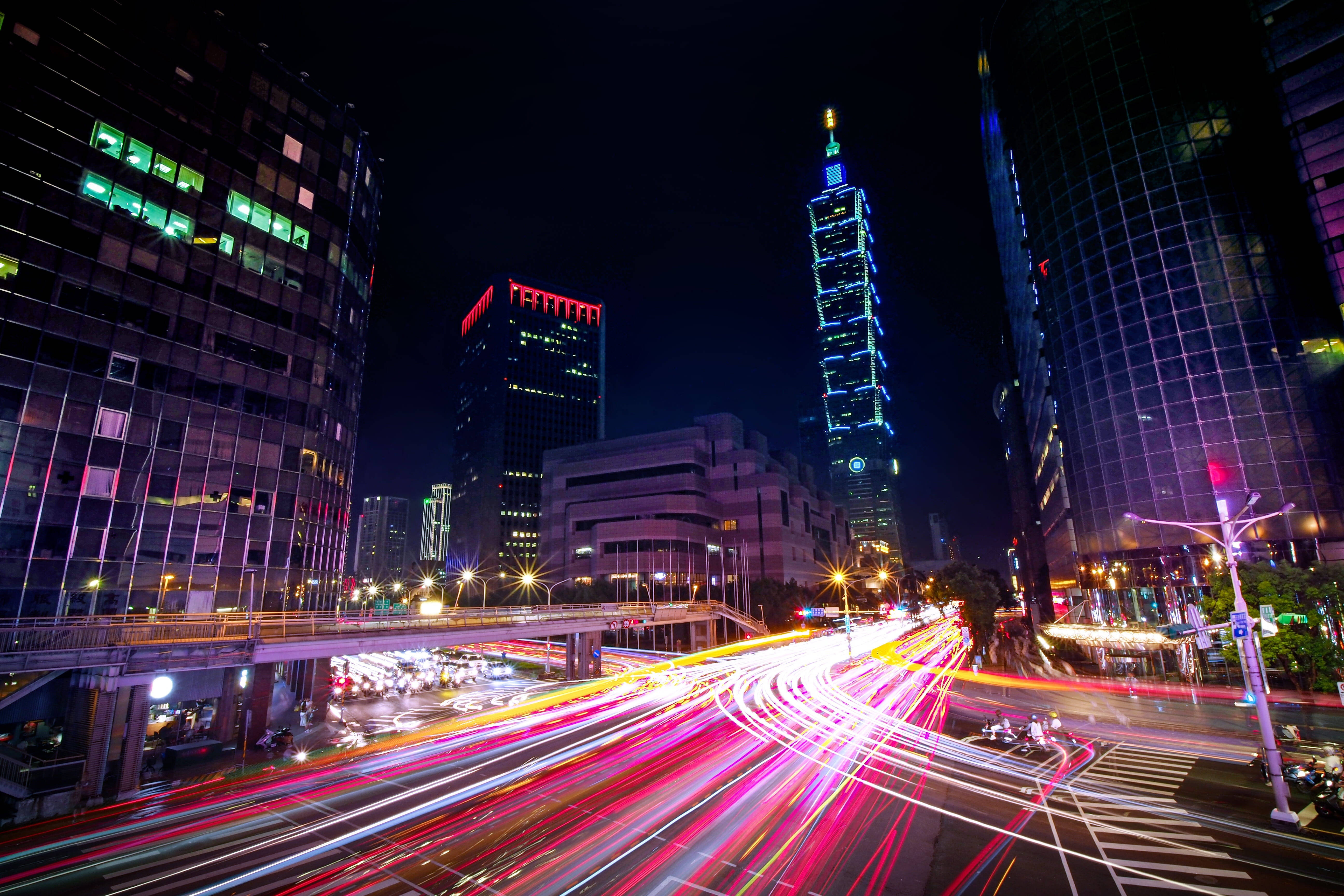 台灣城市延時攝影 壁紙 — 充滿活力的夜景城市景觀，車流在 towering 的 illuminated 摩天大樓下留下光跡。