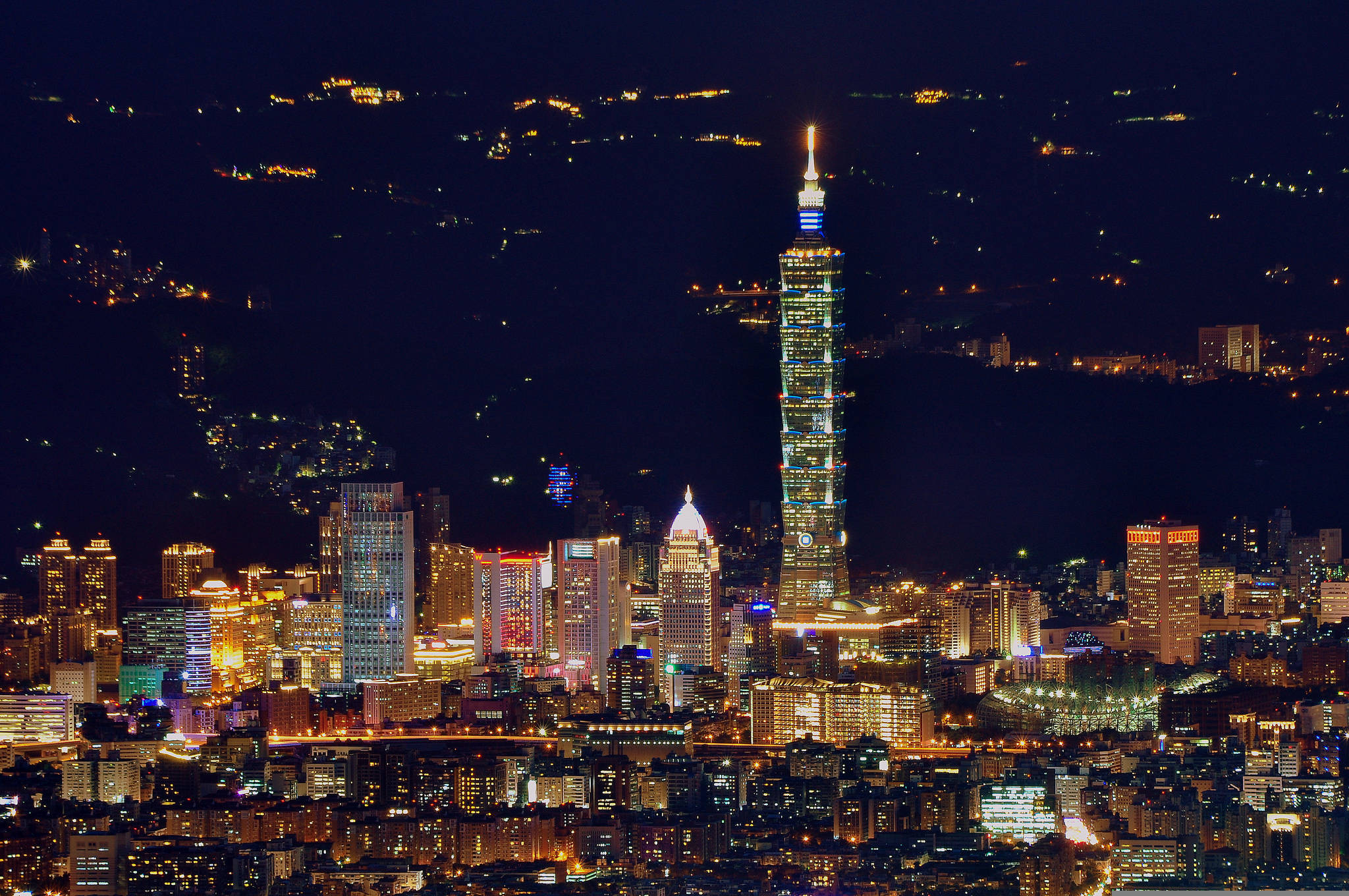 台灣摩天大樓城市 壁紙 — 台北天際線的璀璨夜景，以發光的台北101摩天大樓為主，在黑暗的天空中閃耀。