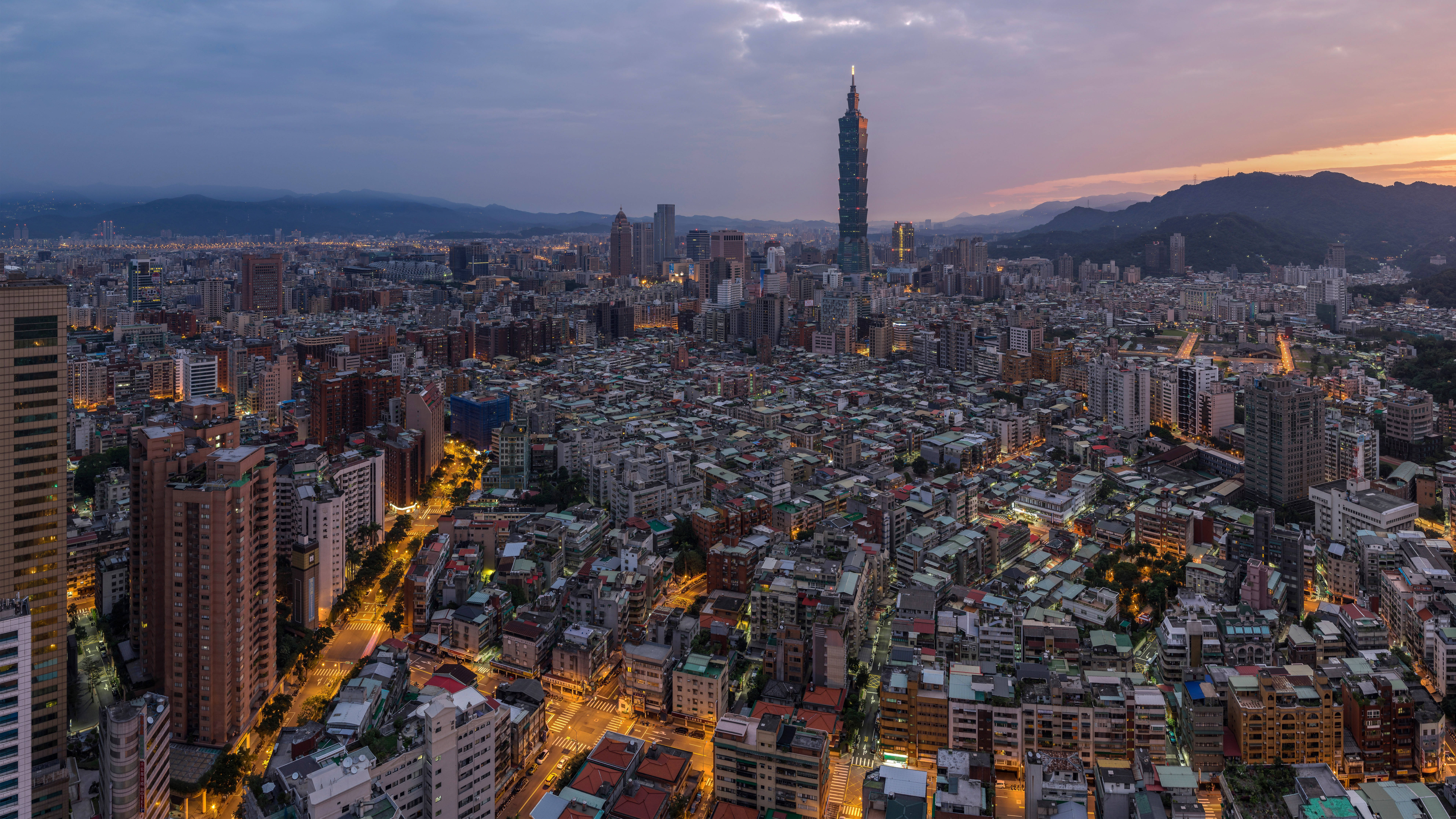 台灣空中鳥瞰 壁紙 — 從高空俯瞰台北市景，黃昏時分街道燈火通明，標誌性的台北101大樓劃破暮色天空。