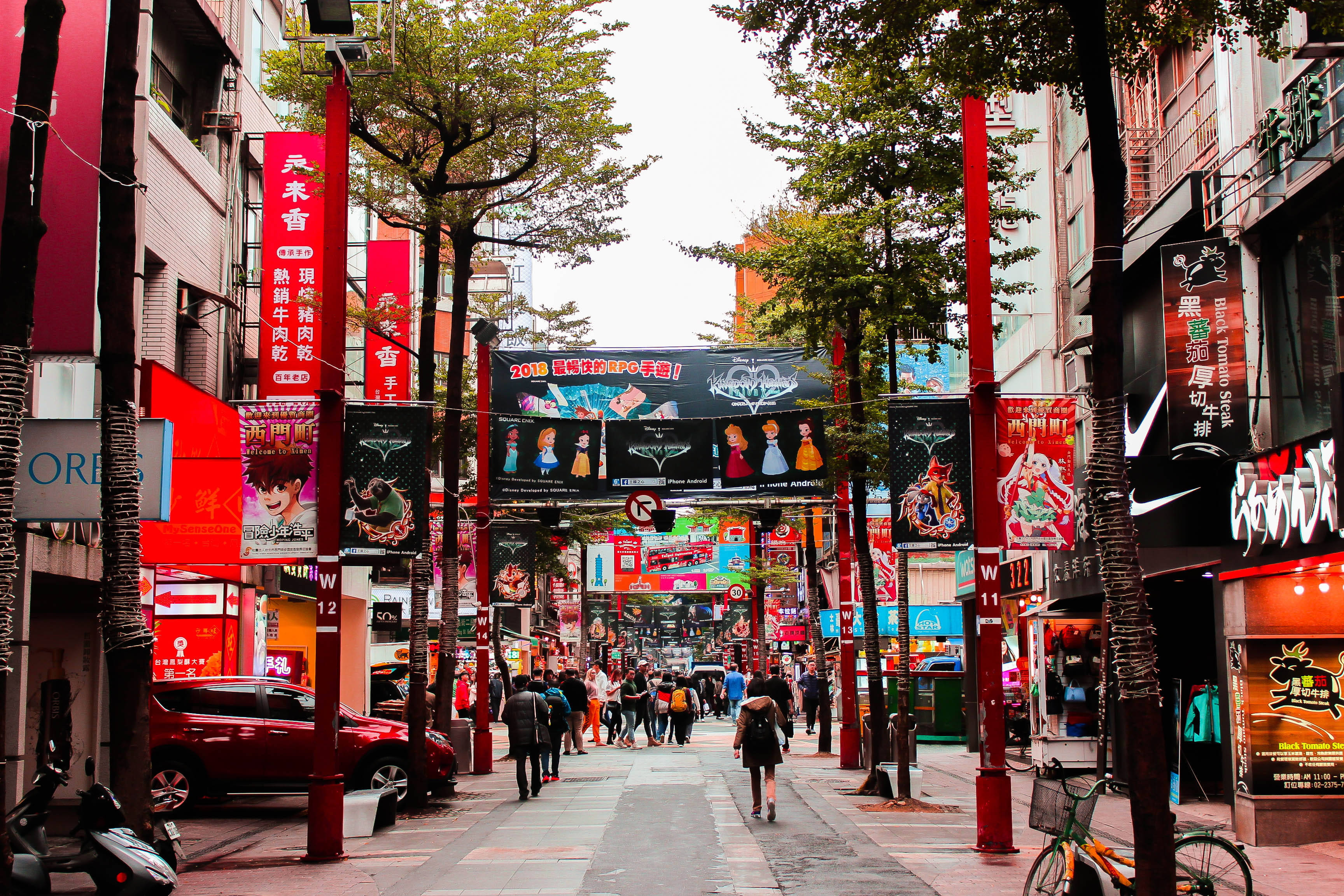 台灣購物區街景 壁紙 — 繁華的商業區街道，色彩繽紛的霓虹招牌和紅色柱子下擠滿行人，充滿活力。