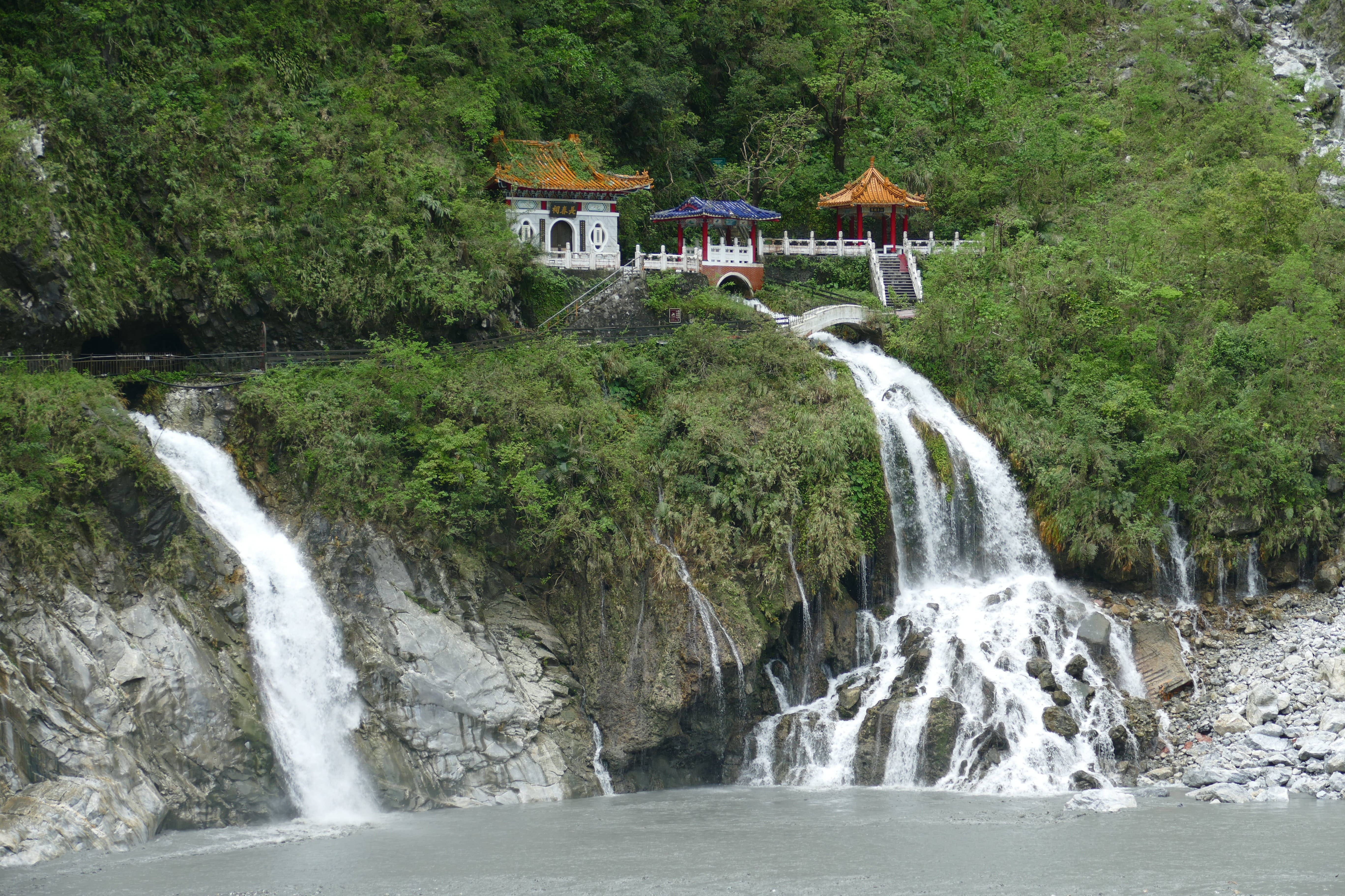 台灣長春祠壯麗風景 壁紙 — 瀑布從岩石懸崖上傾瀉而下，旁邊是鬱鬱蔥蔥的植被，山坡上點綴著傳統中式亭閣。