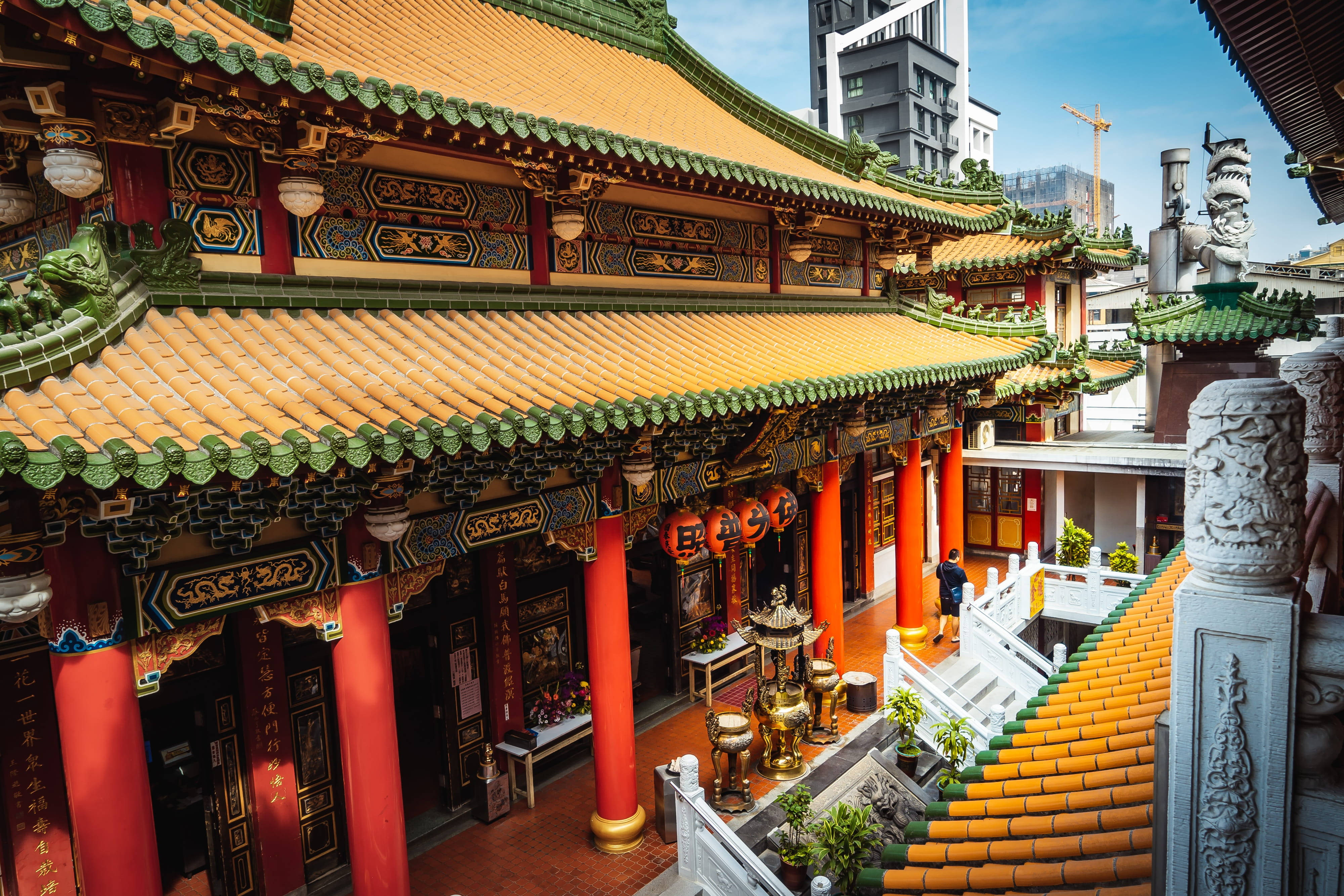 台灣高雄寺廟 壁紙 — 一座充滿活力的傳統中式寺廟，擁有華麗的金色屋頂、紅色柱子和精緻的雕刻，坐落在現代摩天大樓旁。