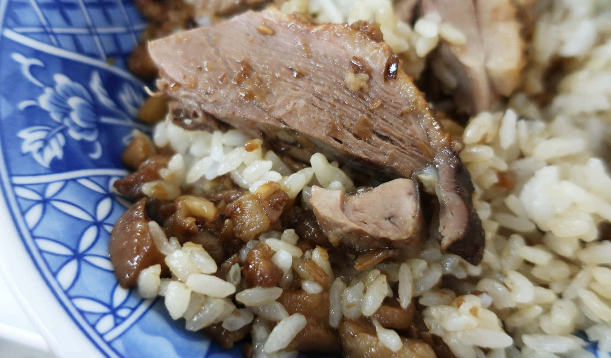 台灣高雄鴨真餐廳必吃鴨肉飯 壁紙 — 藍色花卉陶瓷碗中嫩滑紅燒肉片和米飯的特寫。