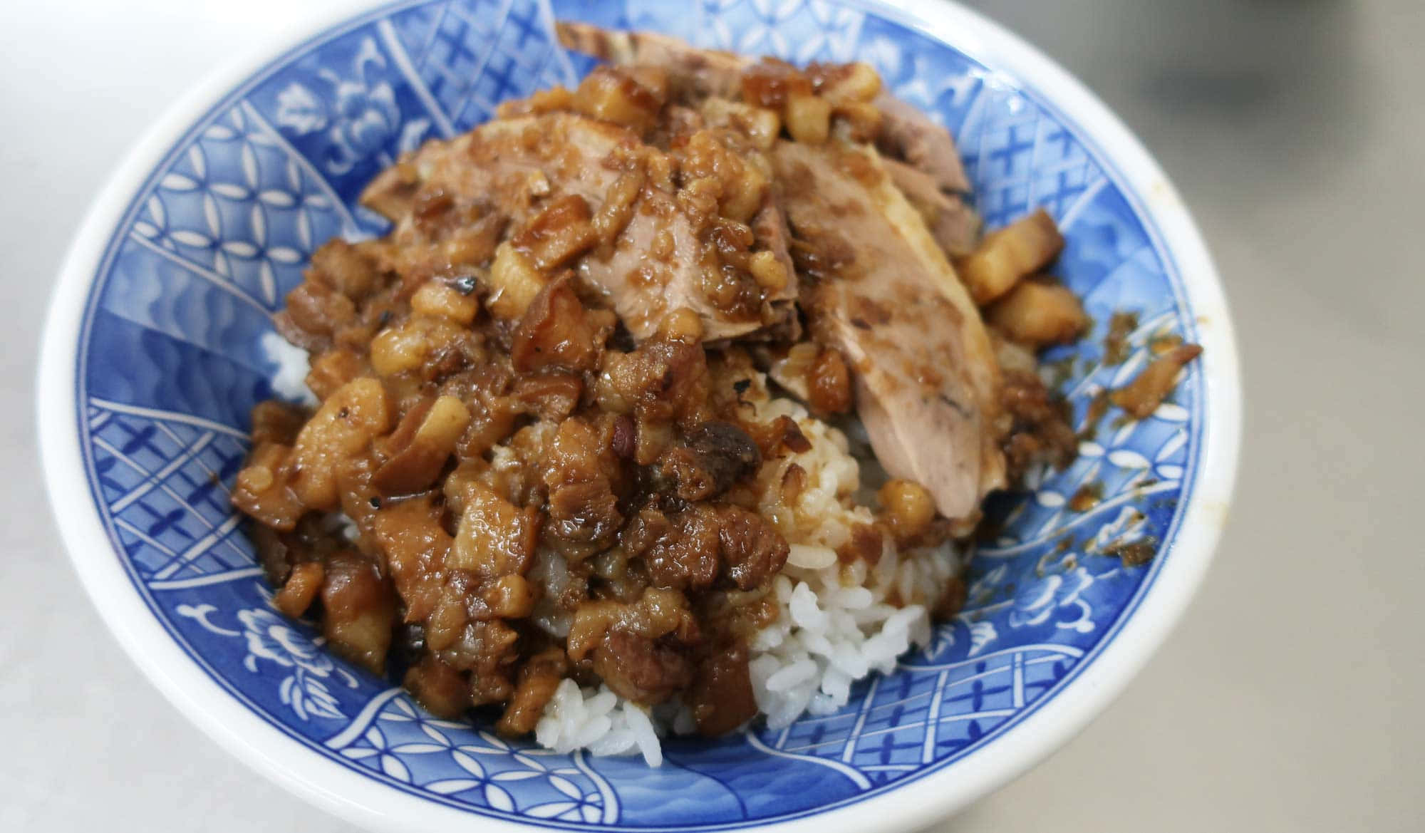 台灣高雄鴨真餐廳招牌鴨肉飯 壁紙 — 一碗藍白圖案陶瓷碗中嘅燜豬肉飯嘅特寫。