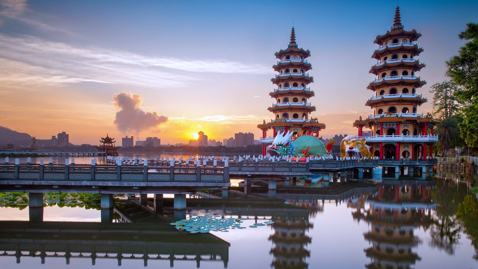 台灣龍虎塔 壁紙 — 兩座華麗的寶塔倒映在平靜的水面上，夕陽在城市天際線後落下。