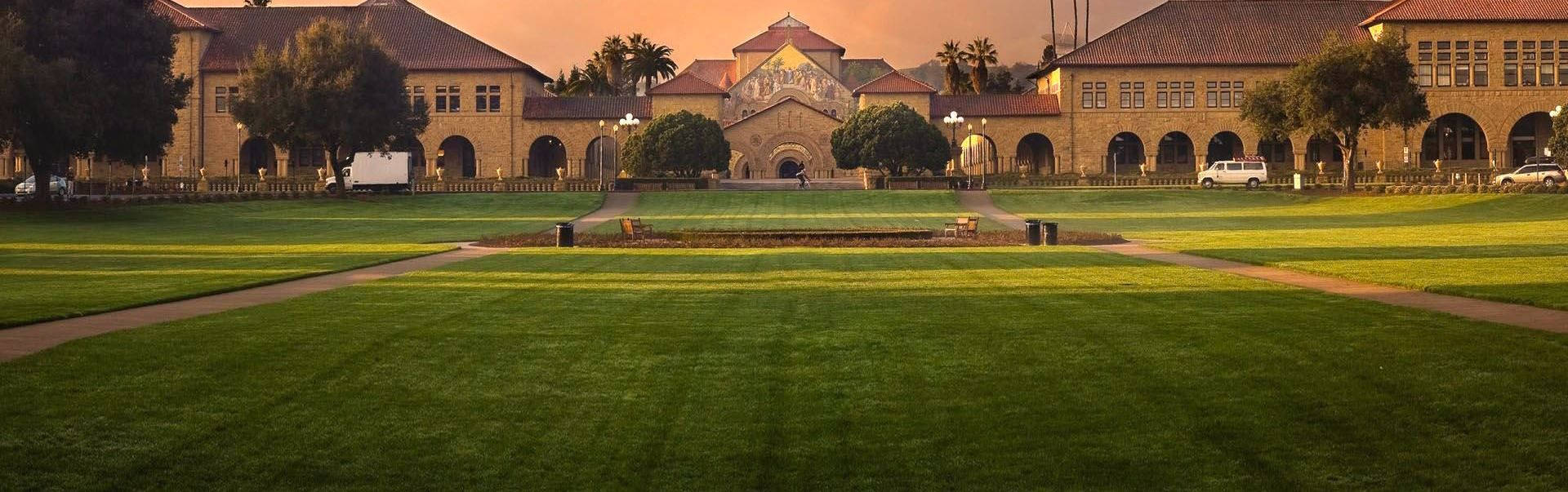 夕陽下的大學校園，金色光芒灑在建築物和綠色草坪上。