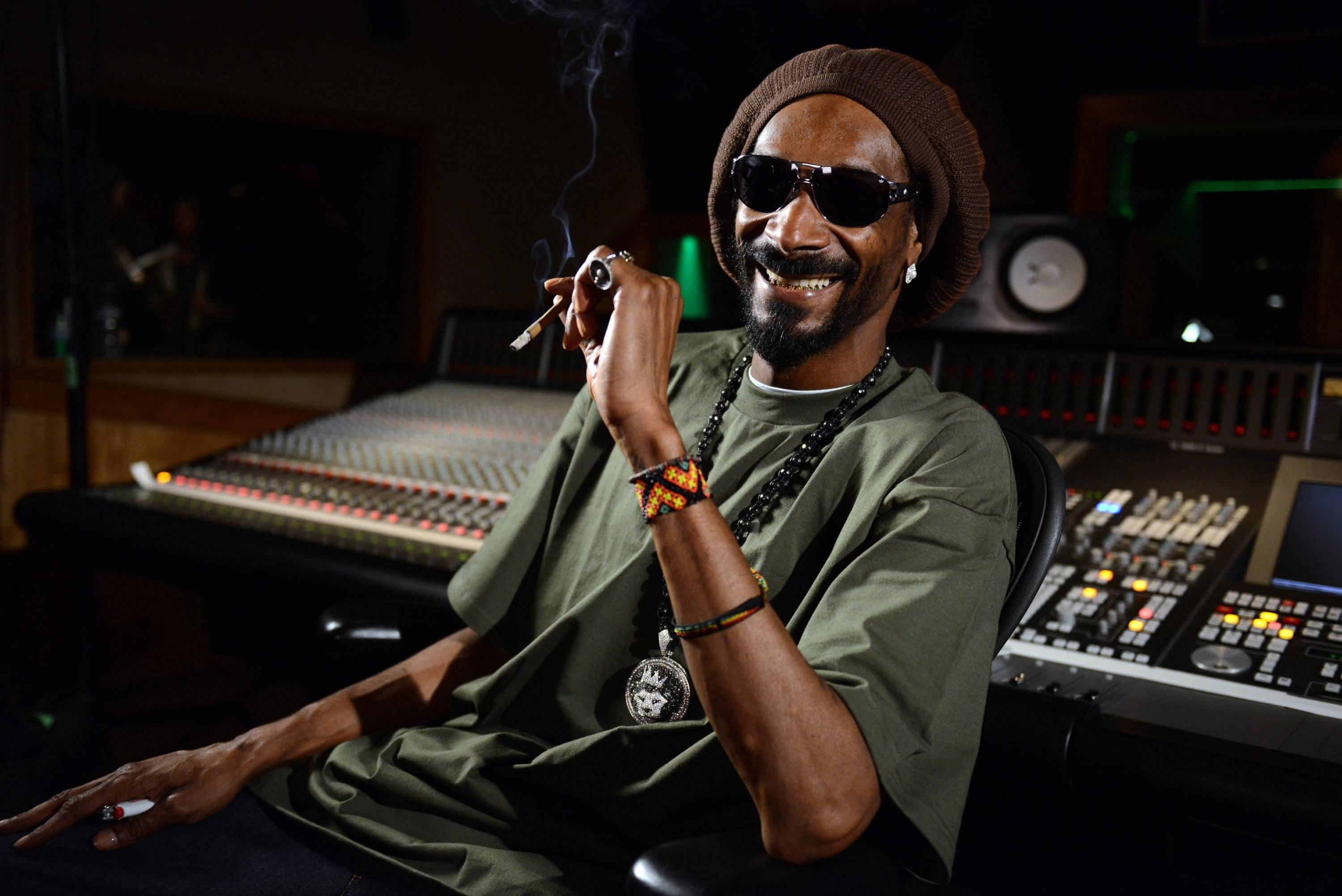 史努比狗在錄音室 壁紙 — Snoop Dogg 在燈光昏暗的錄音室中，被音響設備包圍，一邊吸煙一邊微笑。
