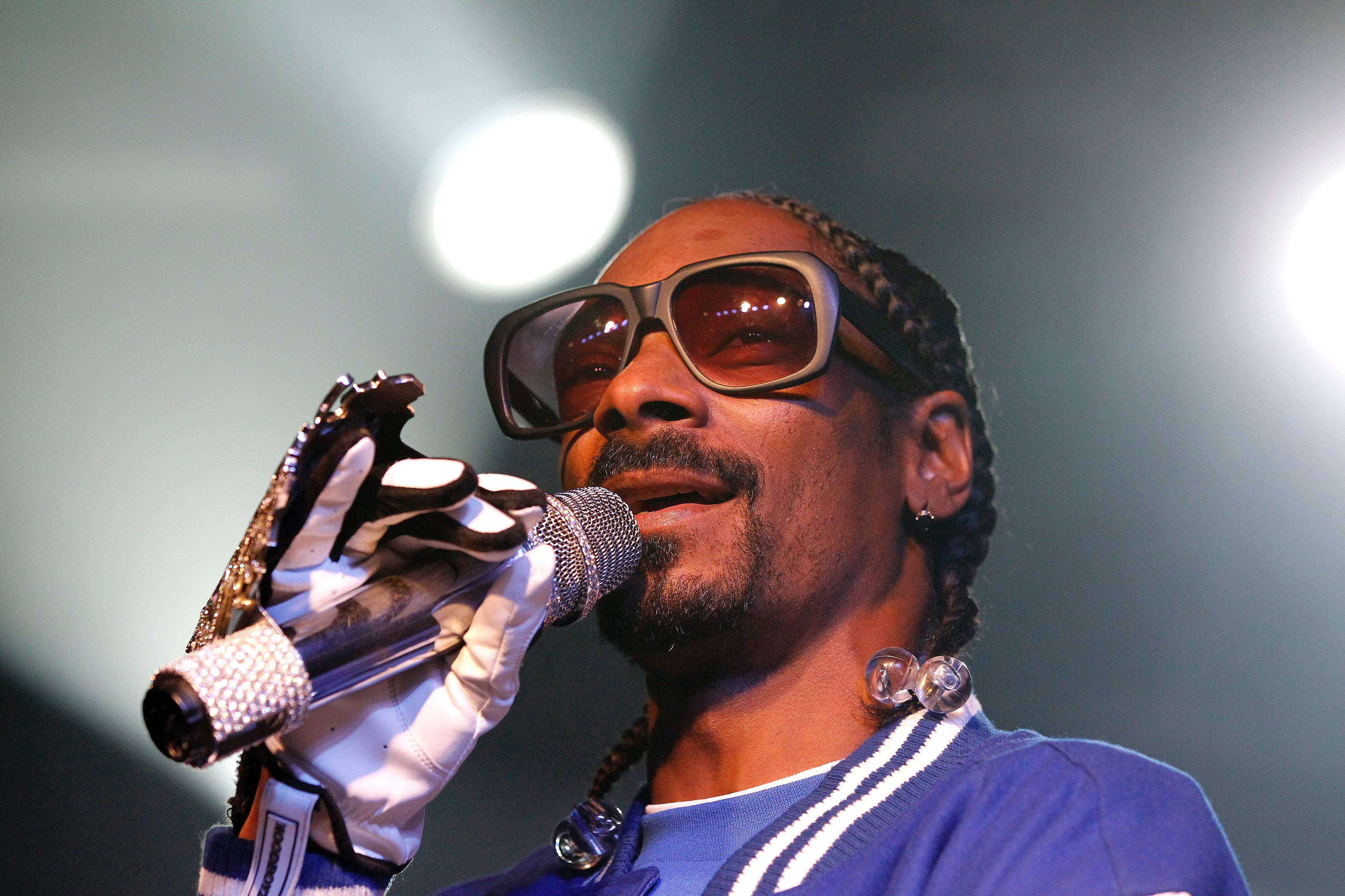史努比狗現場演唱會 壁紙 — Snoop Dogg 在舞台上表演，戴著太陽眼鏡和白色手套，在明亮的舞台燈光下握著麥克風。