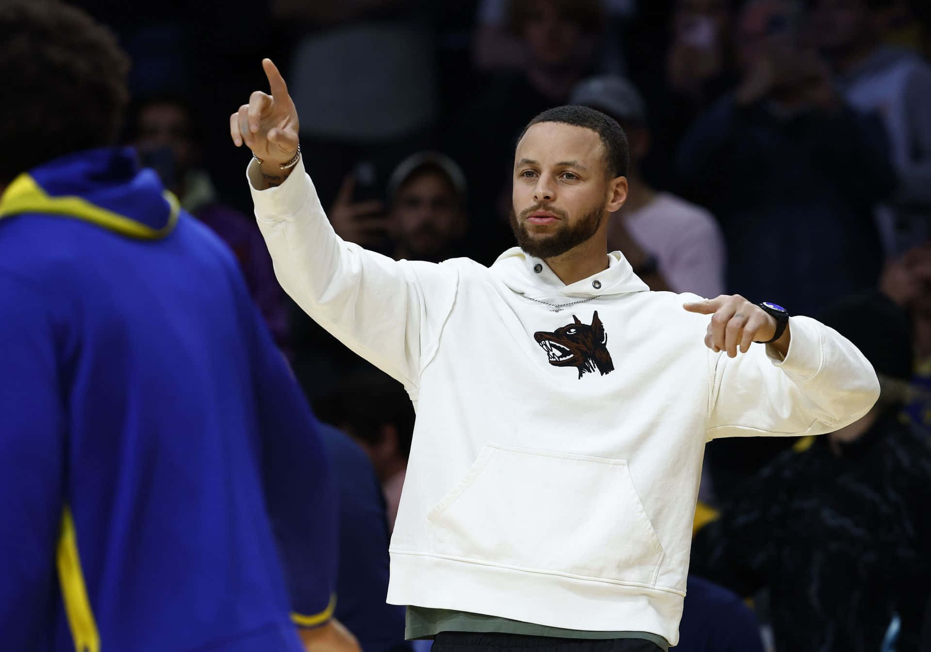 steph curry 桌布 壁紙 — 史提芬居里身穿白色連帽衛衣，在籃球比賽中自信地做手勢，背景是模糊的觀眾。
