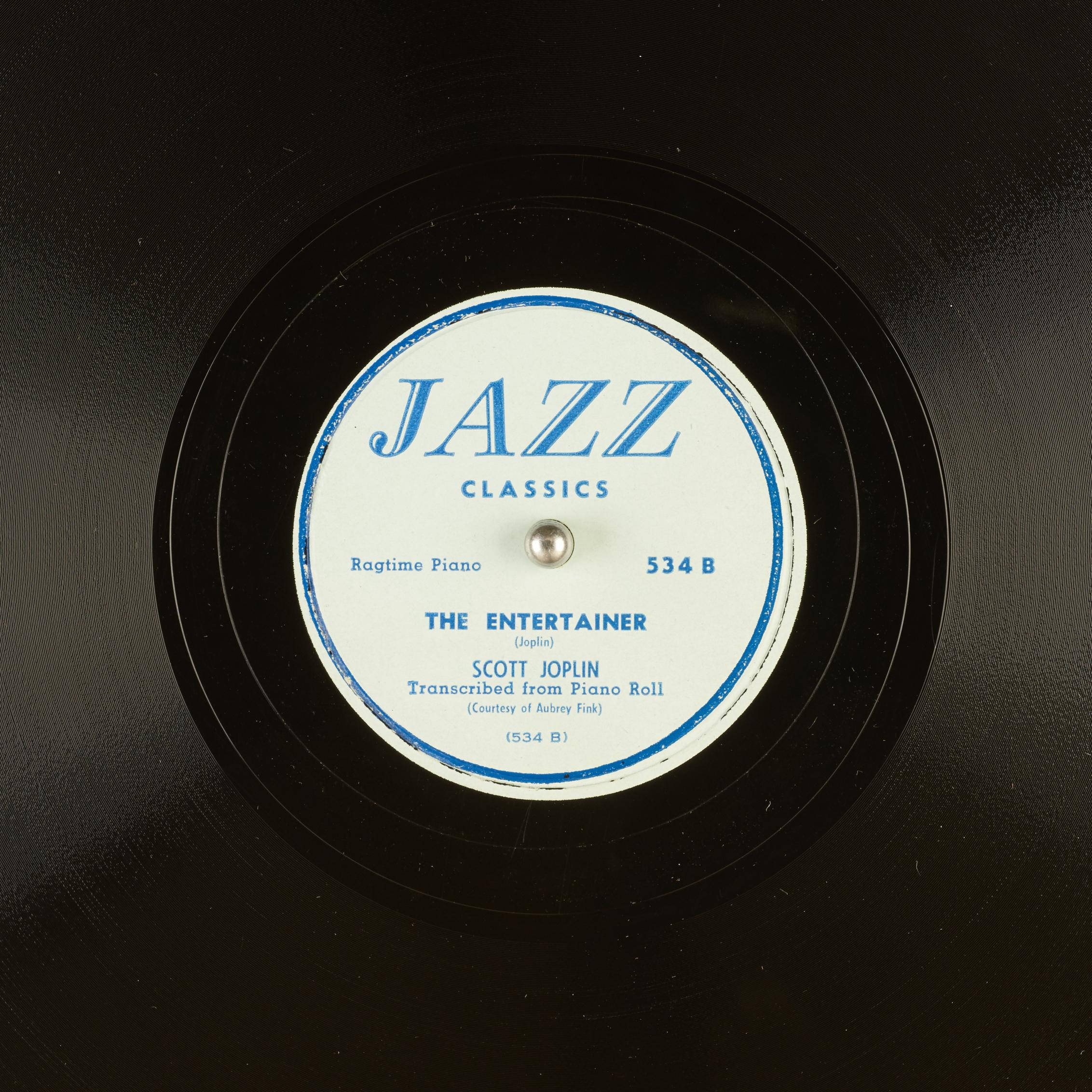 史考特·喬普林《娛樂者》黑膠唱片 壁紙 — Scott Joplin 的《The Entertainer》以粗體藍色文字印在白色中心上的復古爵士黑膠唱片標籤特寫。
