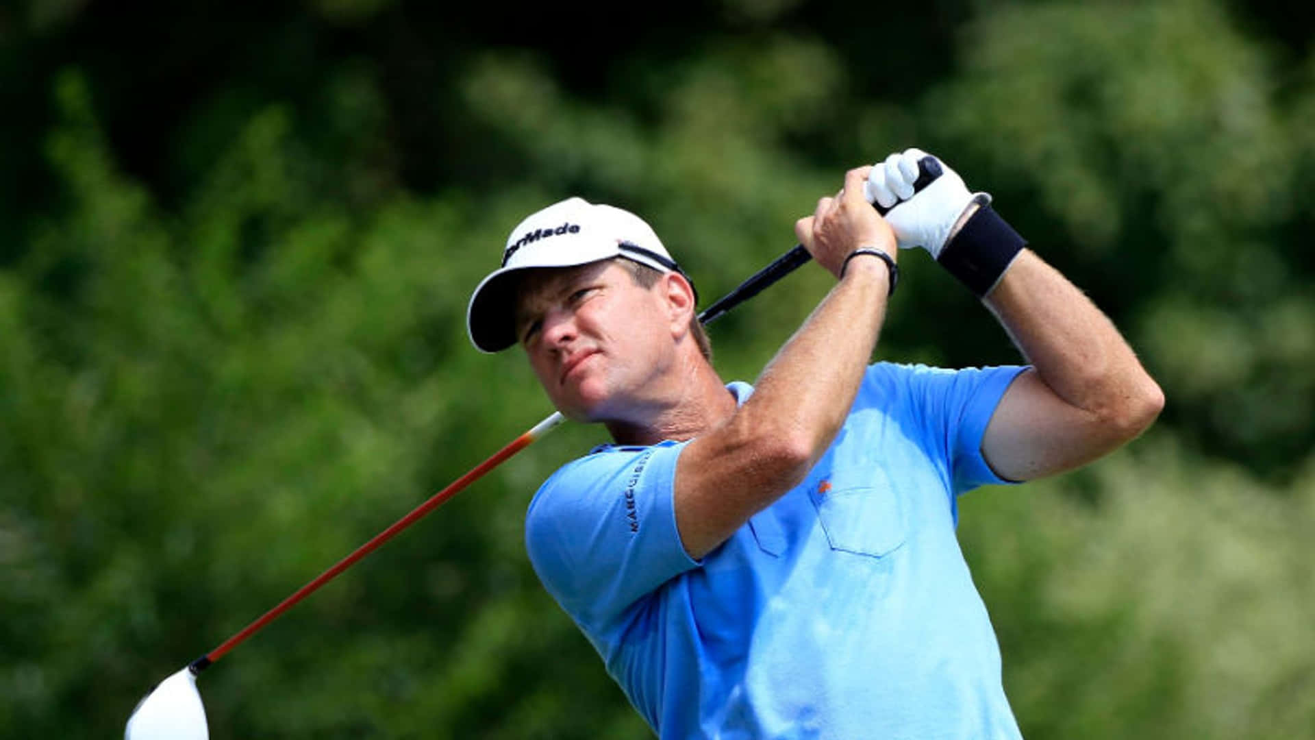 男性高爾夫球手揮桿中，身穿藍色襯衫和白色帽子，戶外。